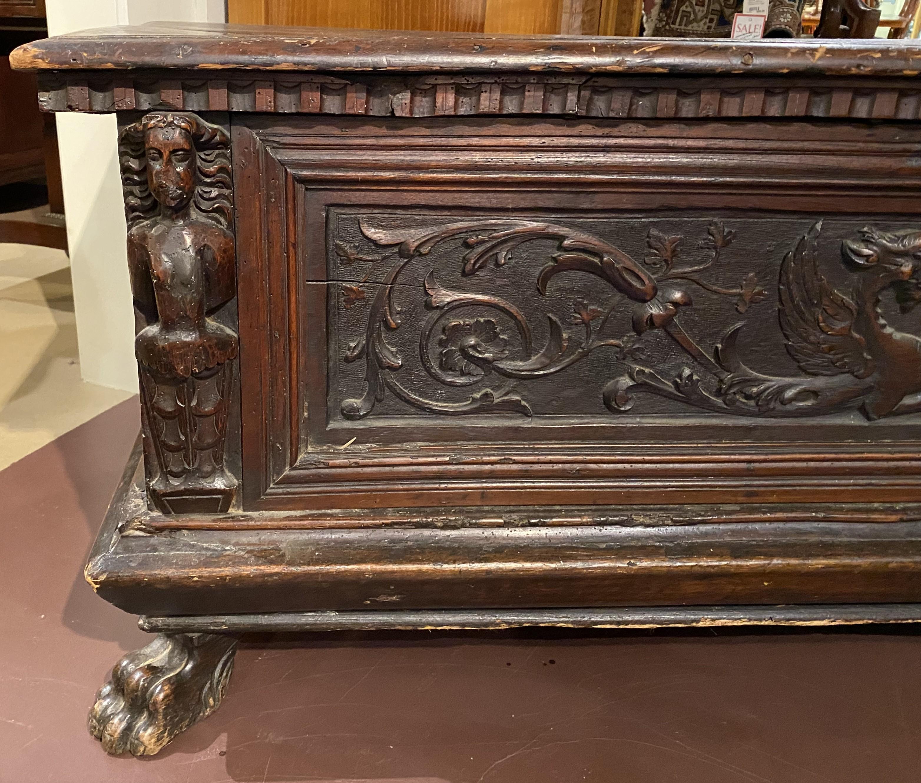 A fine hand carved cassone, probably in oak, with relief carved scrollwork dragons flanking a central shield adorning the front panel, carved figural corners, forged wrought iron strap hinges, an interior till, all supported with two front carved