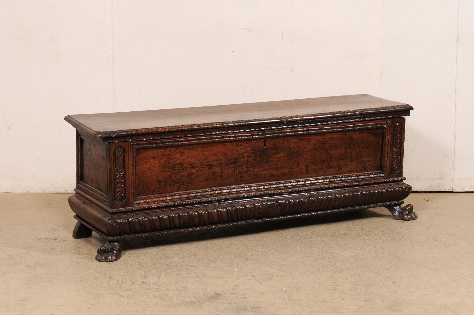 An Italian carved-wood cassone bench with storage from the 18th century. This antique seating bench from Italy has a recessed panel design and front and both short sides; adorned in thickly carved trim and molding with raised oval-shaped foliate