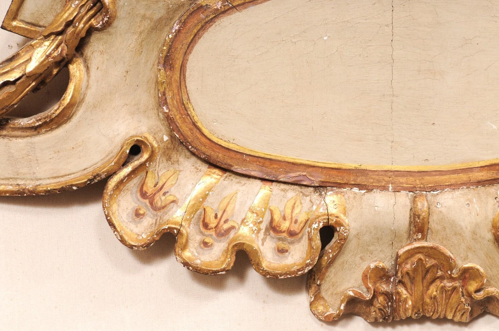 An exquisite 18th century Italian gilded and painted wooden wall plaque. This large size antique wall decoration from Italy features a central cartouche, surrounded by a variety of motifs: reminiscent of the Baroque period, volutes and scrolls flank