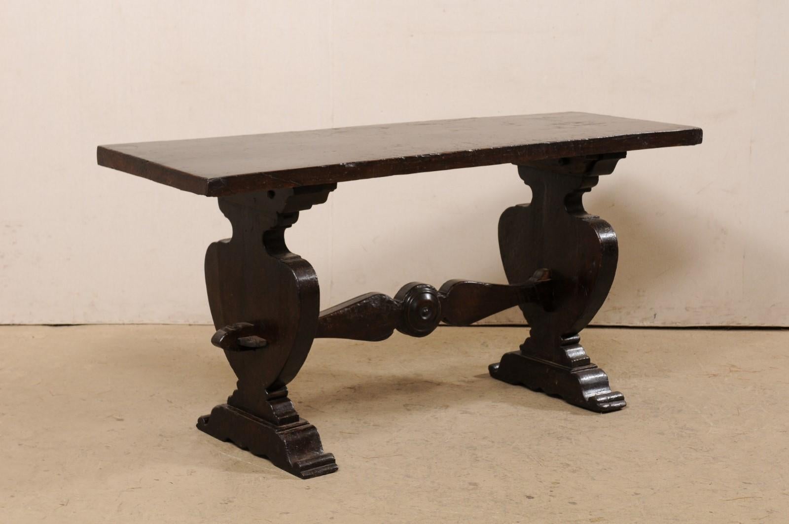 An Italian carved wood trestle table from the 18th century. This antique table from Italy features a single board top, rectangular in shape, which is raised on a pair of urn-shaped legs flanking either side, with stacked rail feet. A beautifully