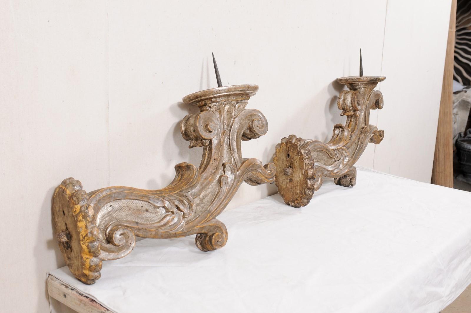 A large Italian pair of carved-wood pricket sconces from the 18th century. This antique pair of candle sconces from Italy have been carved with flower scalloped backplate at wall, which projects outward into a singular, and robust arm carved in an