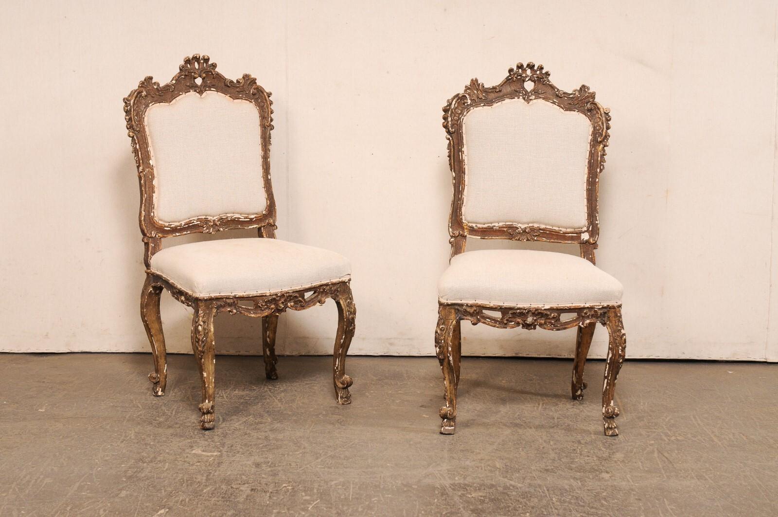 An Italian Venetian pair of richly-carved wood side chairs with upholstered seats from the 18th Century. This pair of antique chairs from Italy are ornately carved throughout with a wonderful scroll, foliate, and shell motif. The top-rail crest,