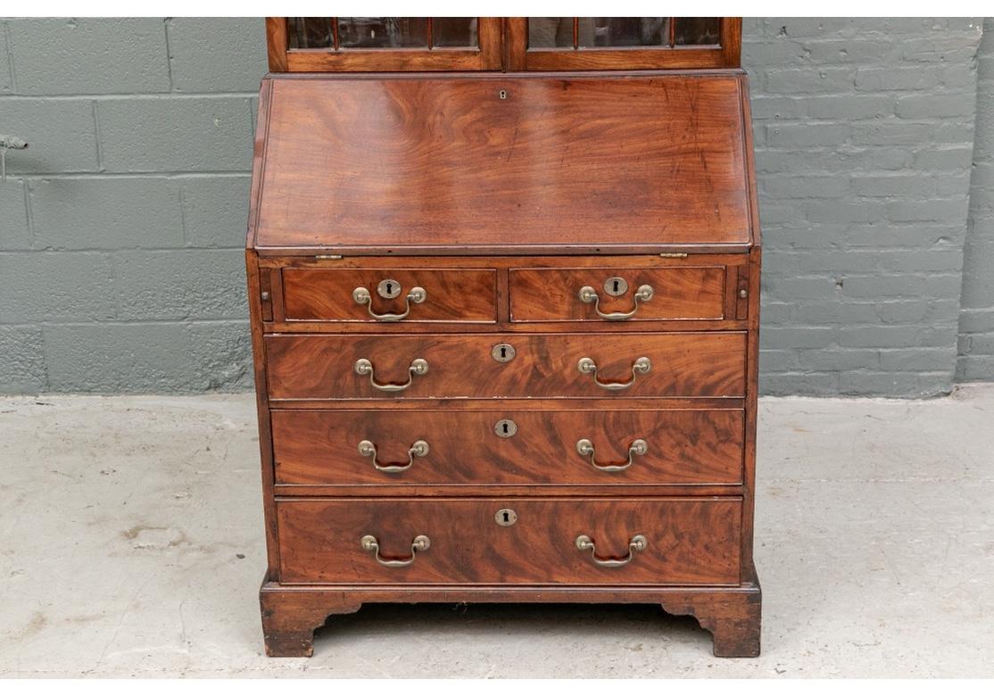 Ca. 1780. A fine figured mahogany classic Georgian secretary bookcase with the broken bonnet in openwork foliate scrolls flanking a fluted short pedestal (it appears that it never had a finial). The double glazed doors with mullions open to two