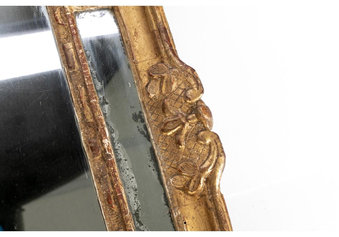 An 18th century segmented mirror with gilt gesso carved wood composition, circa 1720 - 1730. The mirror with arched top and surrounded by rectangular segments. Pierced crest with acanthus leaves and flowers, the crest with a floral urn within two