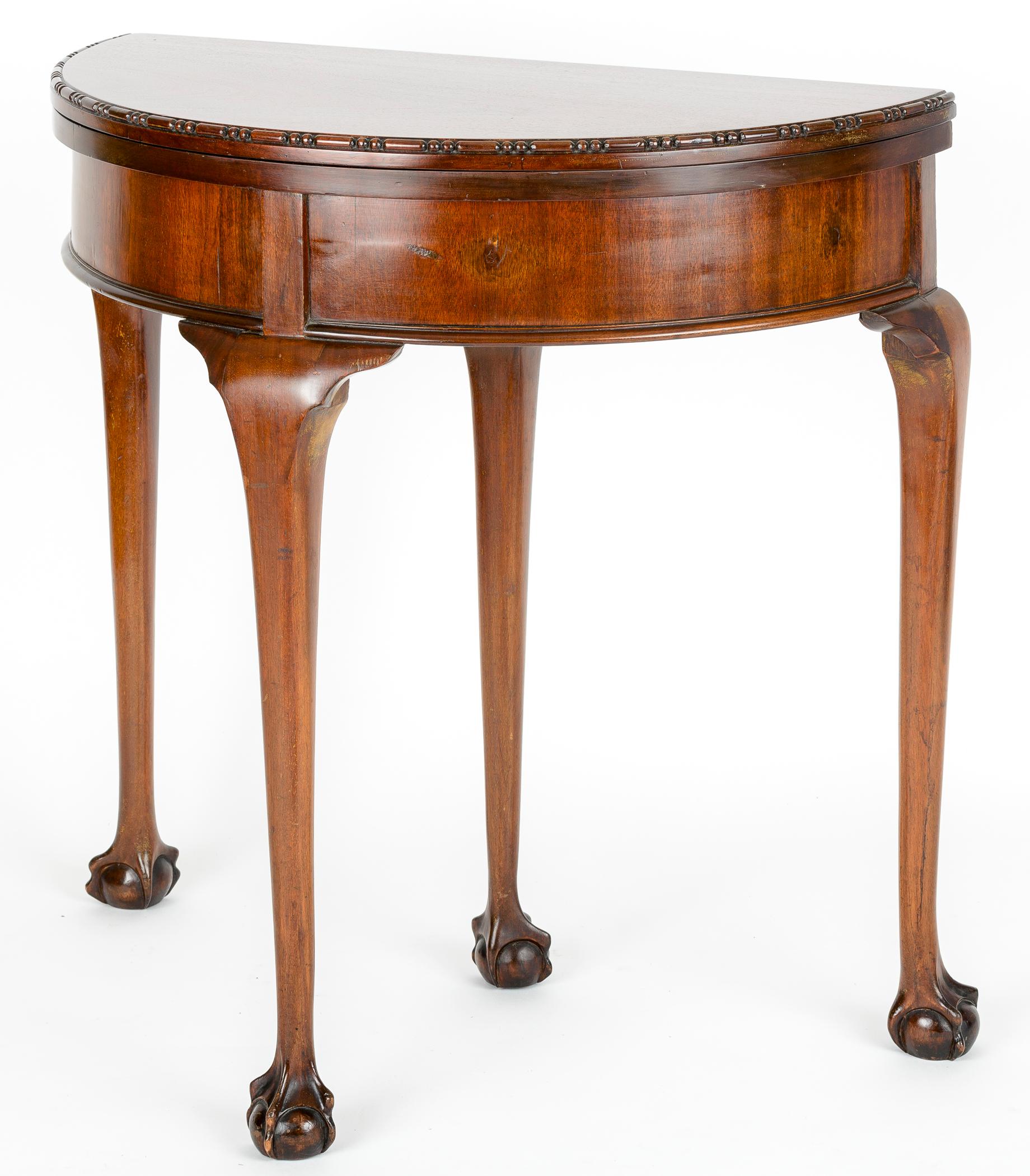 Mahogany demilune game table. The face top has a bead detail edge. The elongated cabriolet legs end in a nicely articulated ball and webbed foot. The fourth leg extends to support the fully opened top.
There is a small secret compartment that is