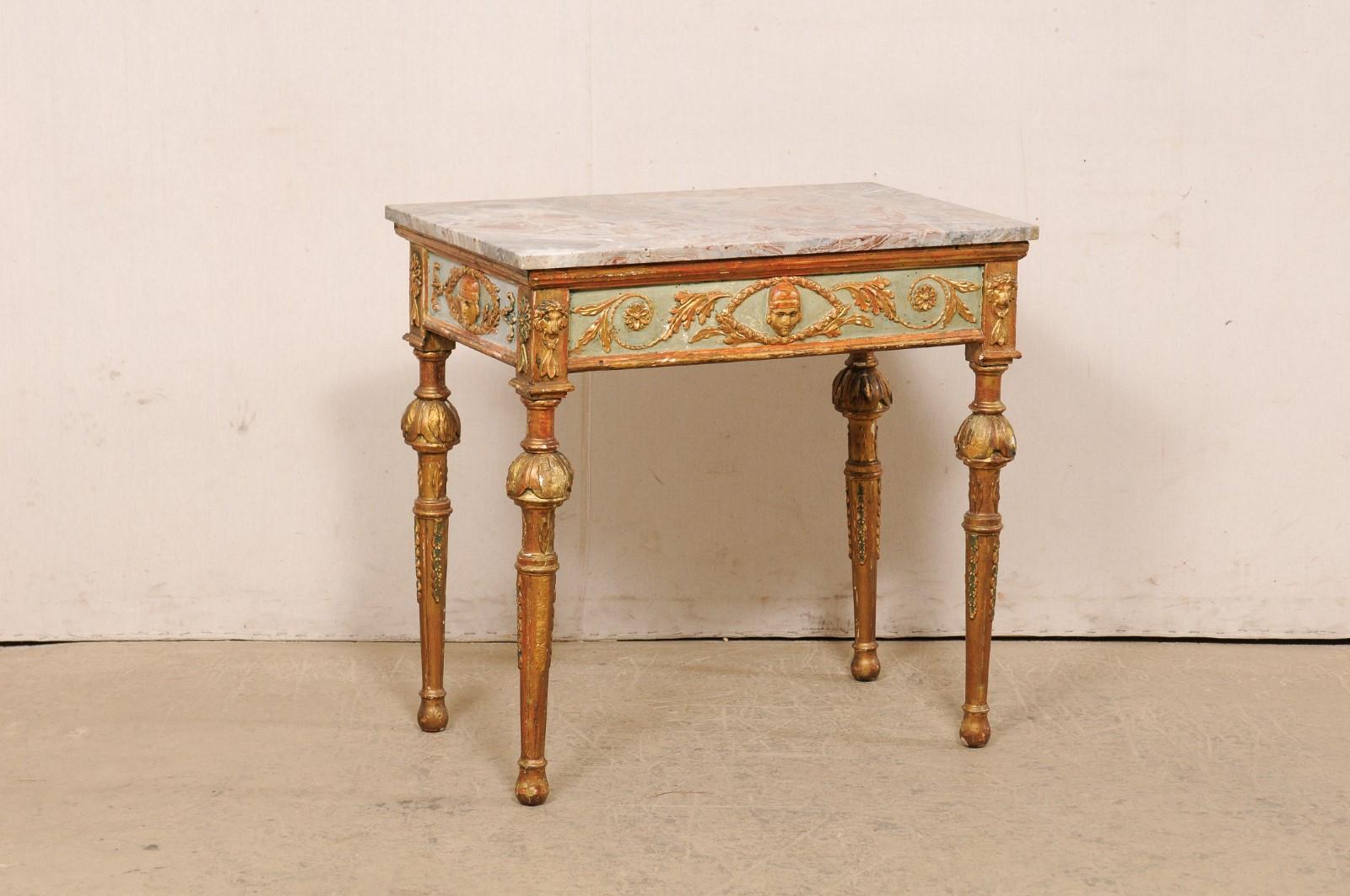 An Italian smaller-sized Neoclassical period carved and painted wood marble top console from the 18th century. This antique table from Italy features a rectangular-shaped marble top, which rests above an apron adorned with a male face within