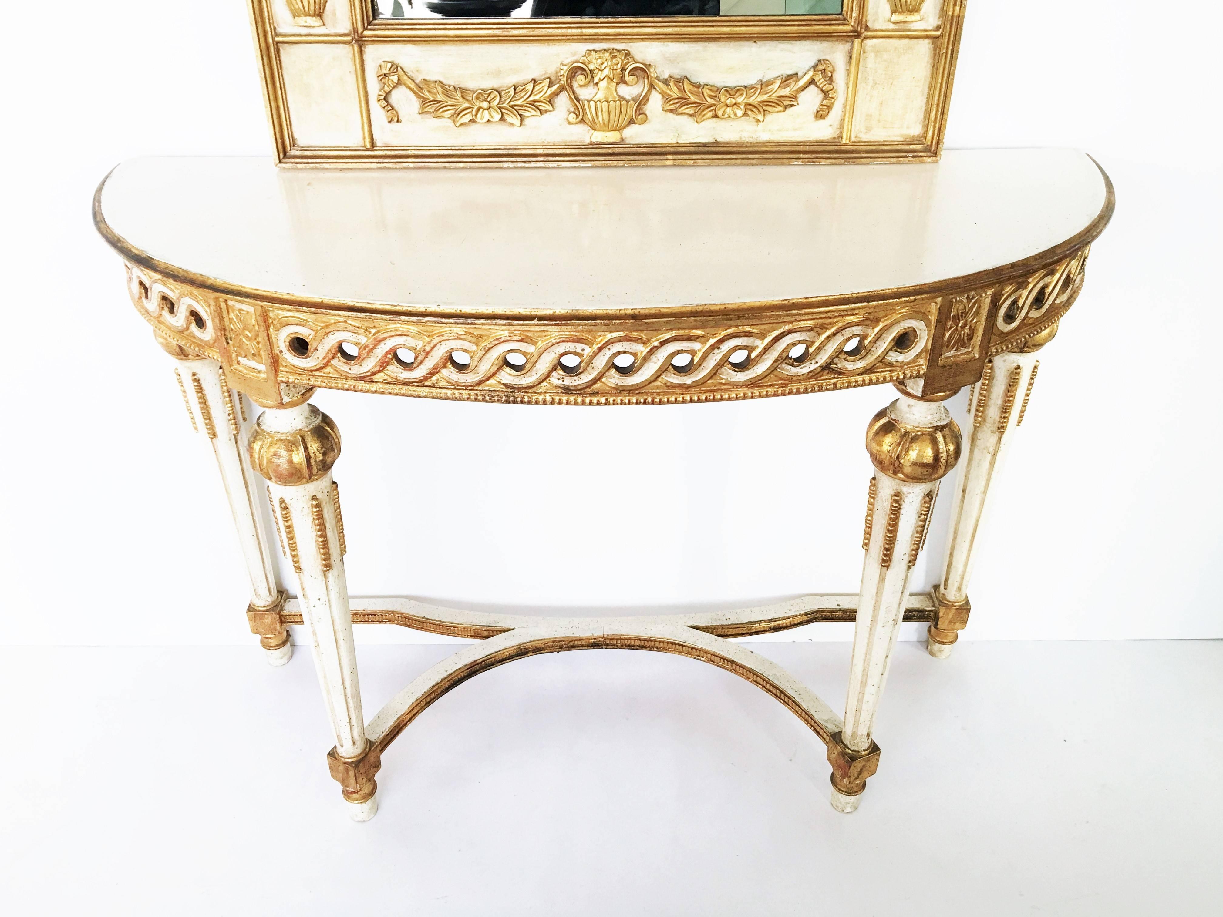 Neoclassical Italian parcel-gilt and painted mirror over console featuring a demilune top over a white painted apron gilt carved with a patterned frieze representing a vitruvian scroll and rosettes on tapered fluted legs. The mirror, exhibiting gilt