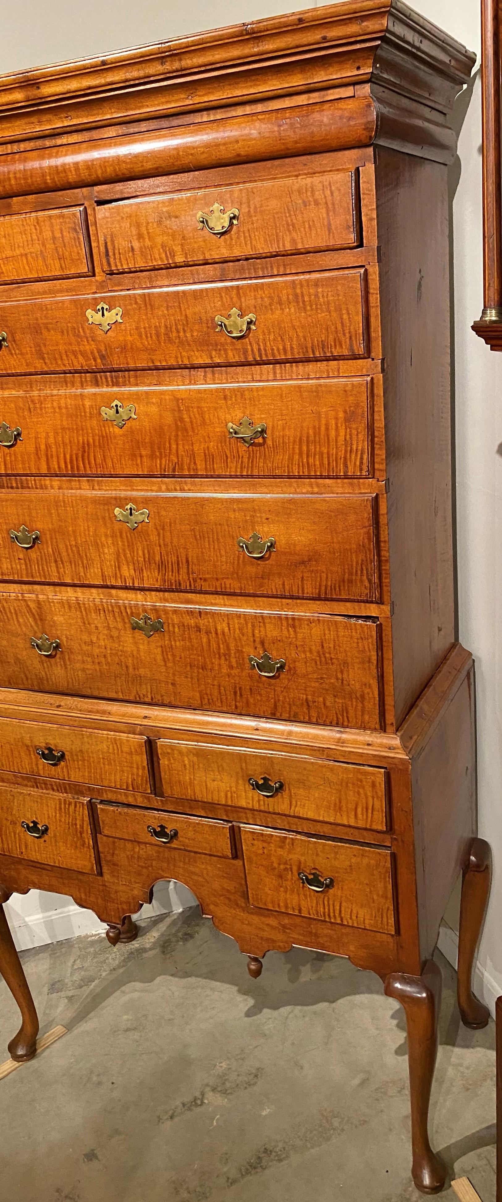A Fine two part New England highboy in tiger maple, its upper case with a molded cornice surmounting a long thin document drawer near the top over two fitted drawers and four graduated long drawers, over a lower case with waistmolding over five