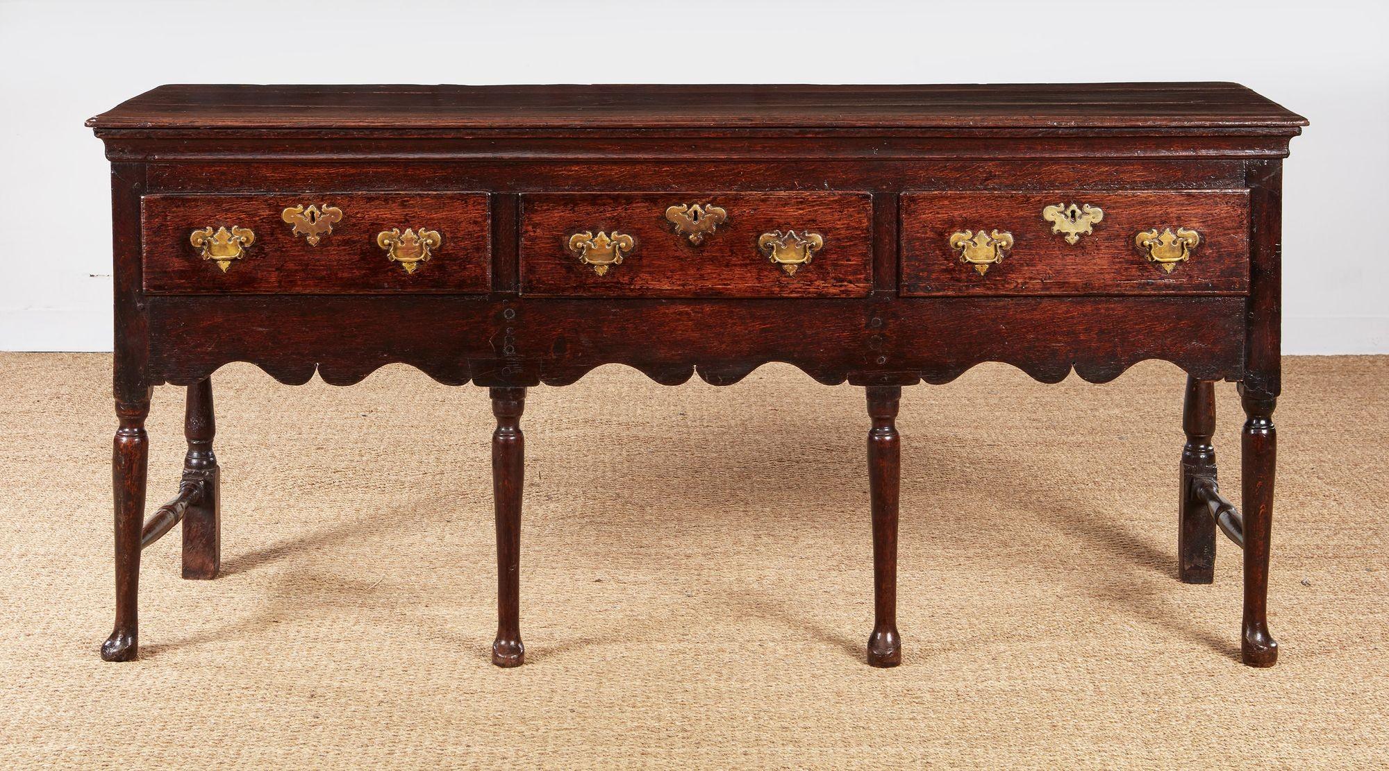 A circa 1720 Welsh oak low dresser having three deep drawers under a slightly overhanging molded edge top on paneled ends, standing on four pad foot legs with two turned and blocked legs to the back joined by front to back turned stretchers to the