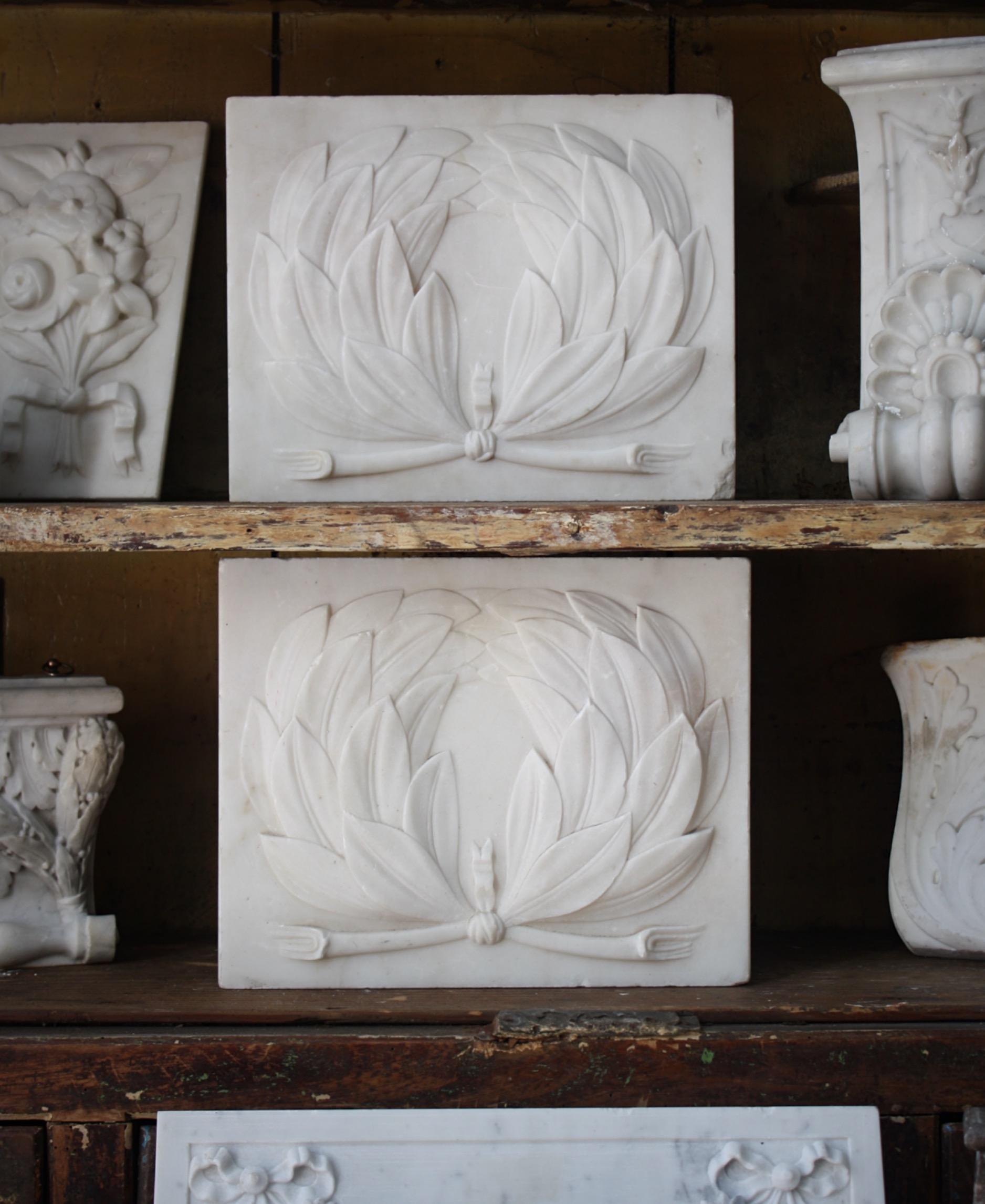 A fine pair of carved marble tablets/architectural elements with delicately carved organic decorations, depicting a laurel wreath a prominent image from Greek history, the tablets previously part of larger feature like a grand fireplace.

The pair