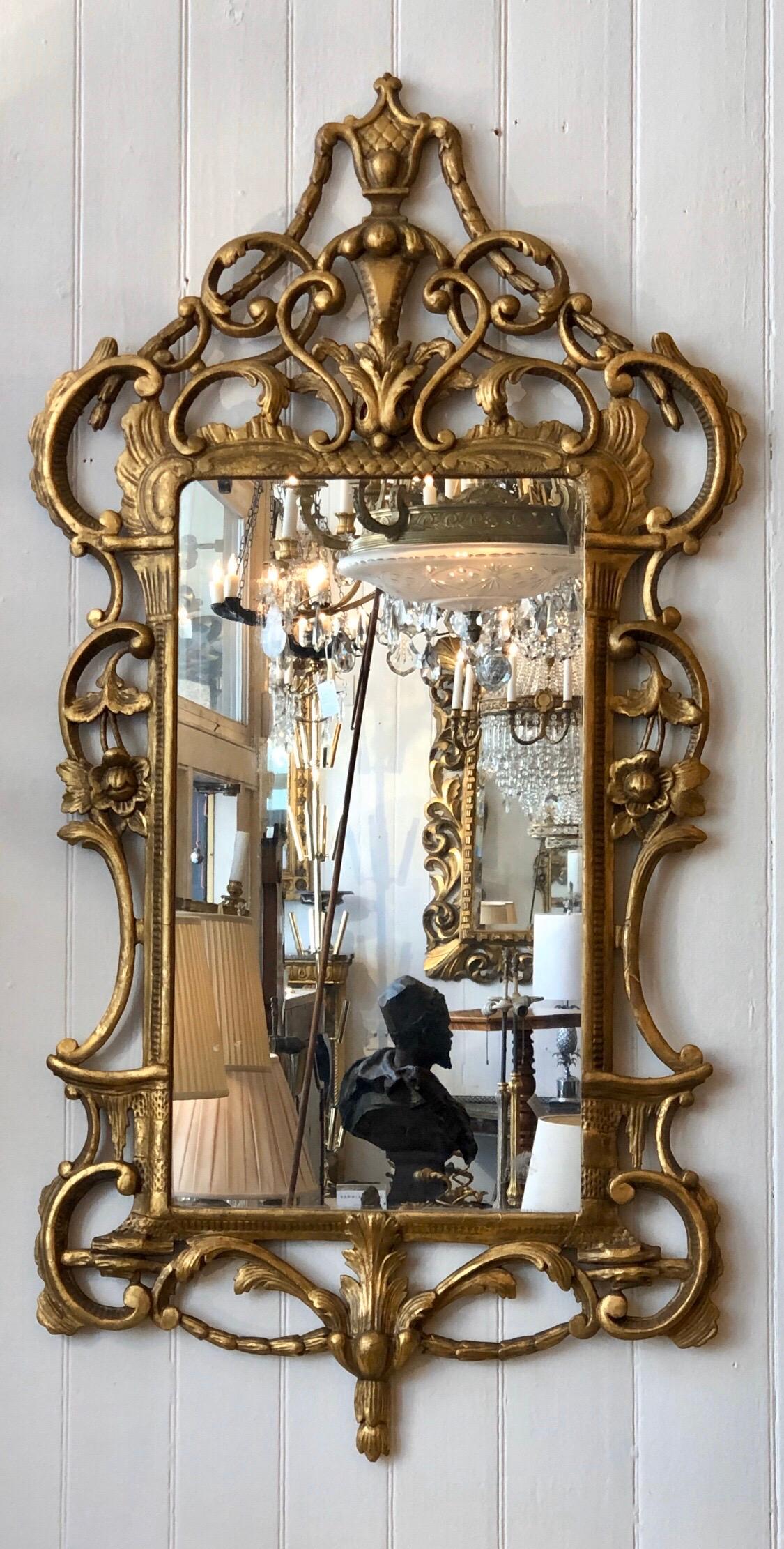 The George III mirrors have Chippendale chinoiserie influences going into the Adams taste. The gilded wood frame has an urn finial ornament crest with bell-flower garlands coming down to cabochon on the corners. The looking glass is framed with