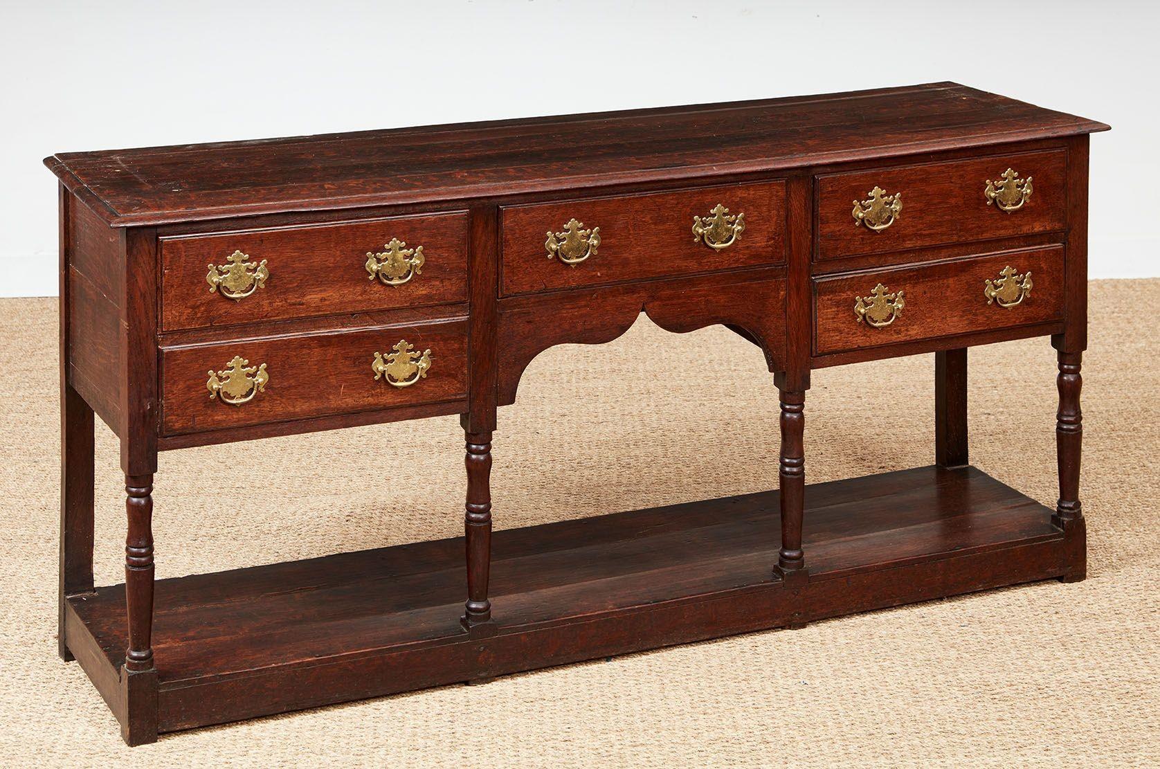 A mid-18th century dresser base with glowing patina in quarter sawn oak having a molded edge top on six turned legs with a bank of double drawers to each side of a central drawer on a boldly scalloped apron over a lower shelf known as a potboard. 