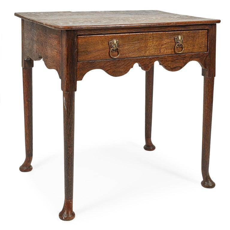An early 18th c. English side table having a single drawer over a scalloped apron to front and sides, standing on tall turned tapering legs ending in circular flattened feet.  Two plank oak top with heightened grain.  Elegant proportions and stance.
