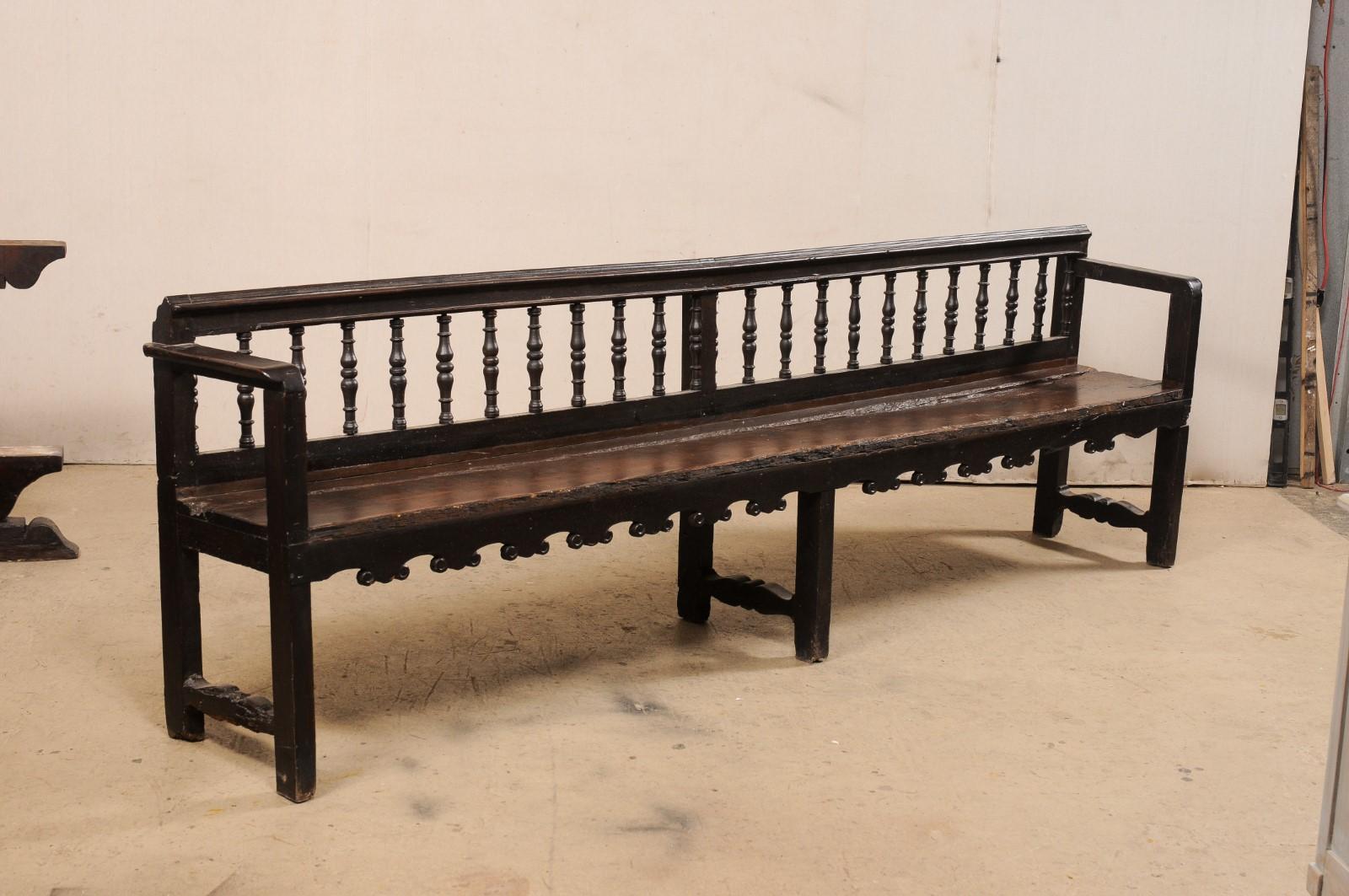 A Spanish carved-wood, spindle back bench from the 18th century. This antique wooden bench from Spain features a linear molded top chair rail with nicely-turned spindles set within the back rests, straight arms flank either side of the rustic