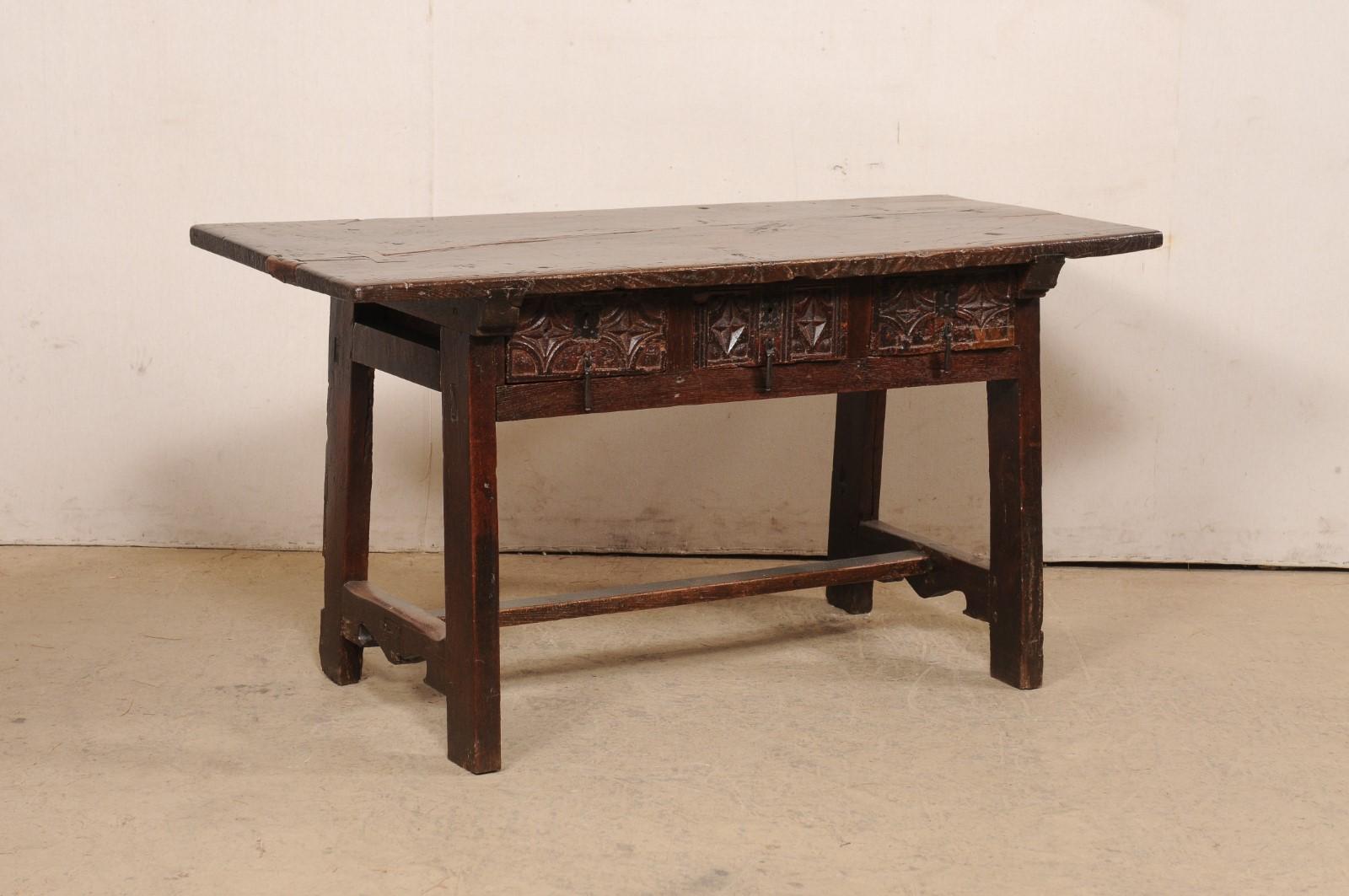 A Spanish carved wood table with drawers from the 18th century. This antique table from Spain has a rectangular-shaped top (beautifully aged with old butterfly repairs) which overhangs the apron below that houses three smaller-sized drawers at one