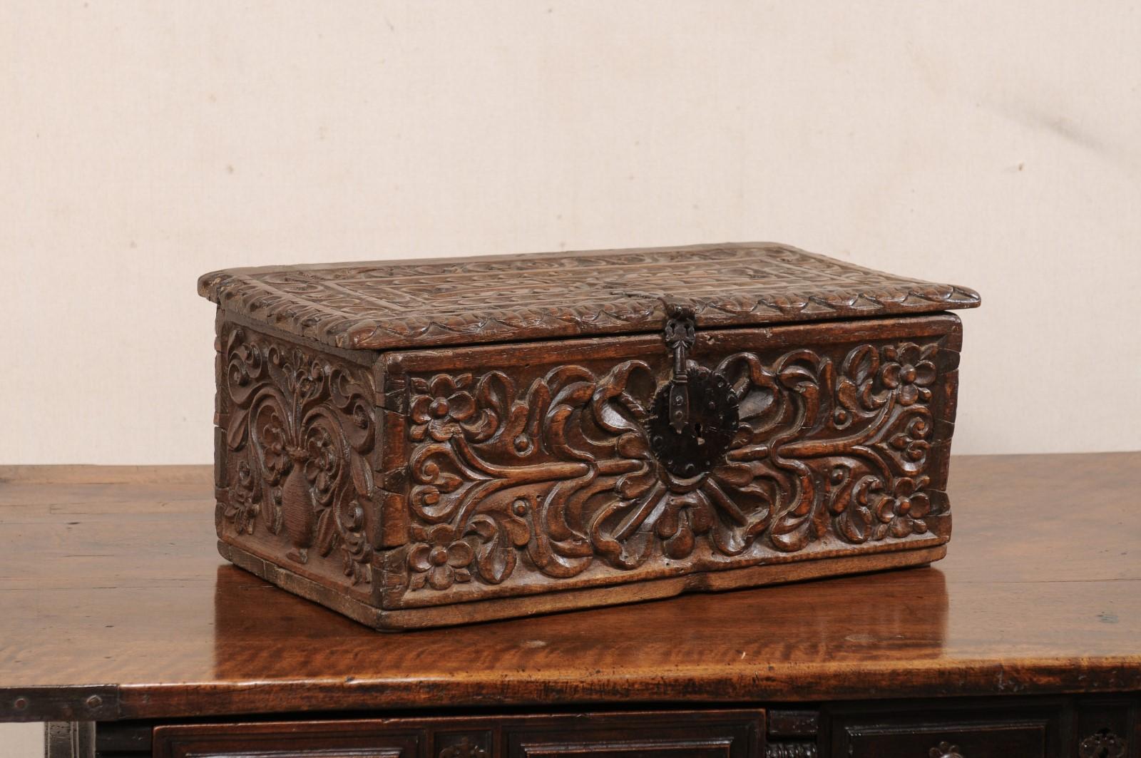 A Spanish Colonial carved-wood storage box from the 18th century. This antique Spanish Colonial period chest has rectangular shape with flat topside, which has been adorned with heavy foliate theme hand-carvings about the top and all four sides