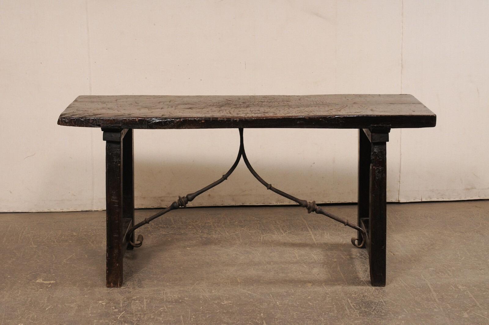 A Spanish trestle-leg wooden table, with decorative forged-iron stretcher, from the 18th century. This antique table from Spain features a solid, rectangular-shaped top, which is raised upon a pair of saw-horse style legs, with a wood beam