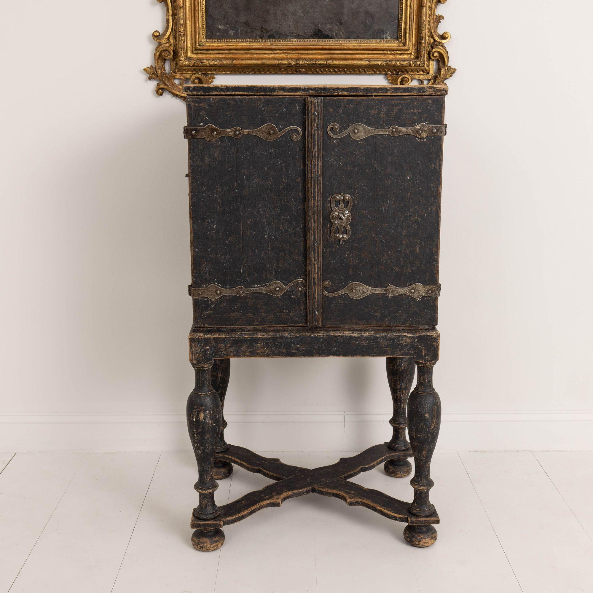 A rare find. A black painted Swedish spice cabinet on stand from the Baroque period. All original hand-forged hardware. The cabinet is raised upon a stand with a carved cross stretcher base. Behind the doors are a series of drawers used to store
