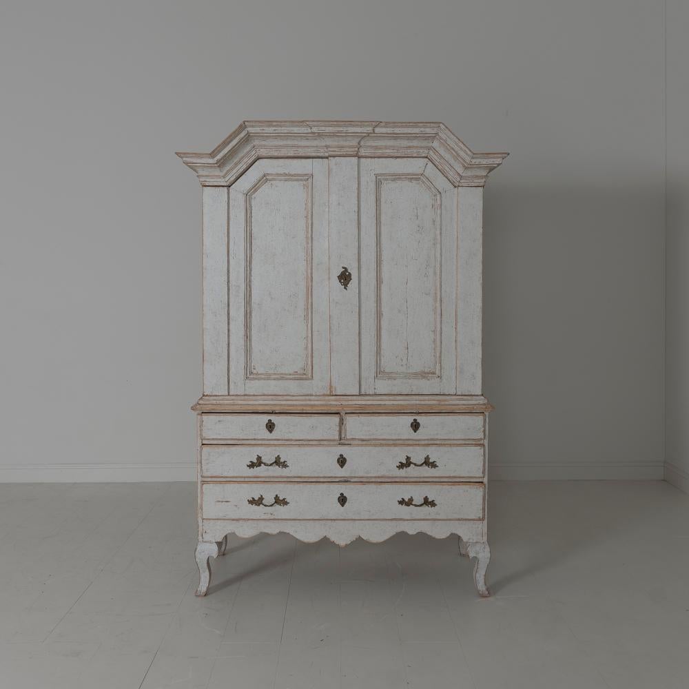 An 18th century three-part Swedish linen press or armoire from the Baroque period with original bronze hardware, locks, and keys. This cabinet is beautifully proportioned with a shaped pediment cornice and curvaceous cabriole legs. The antique