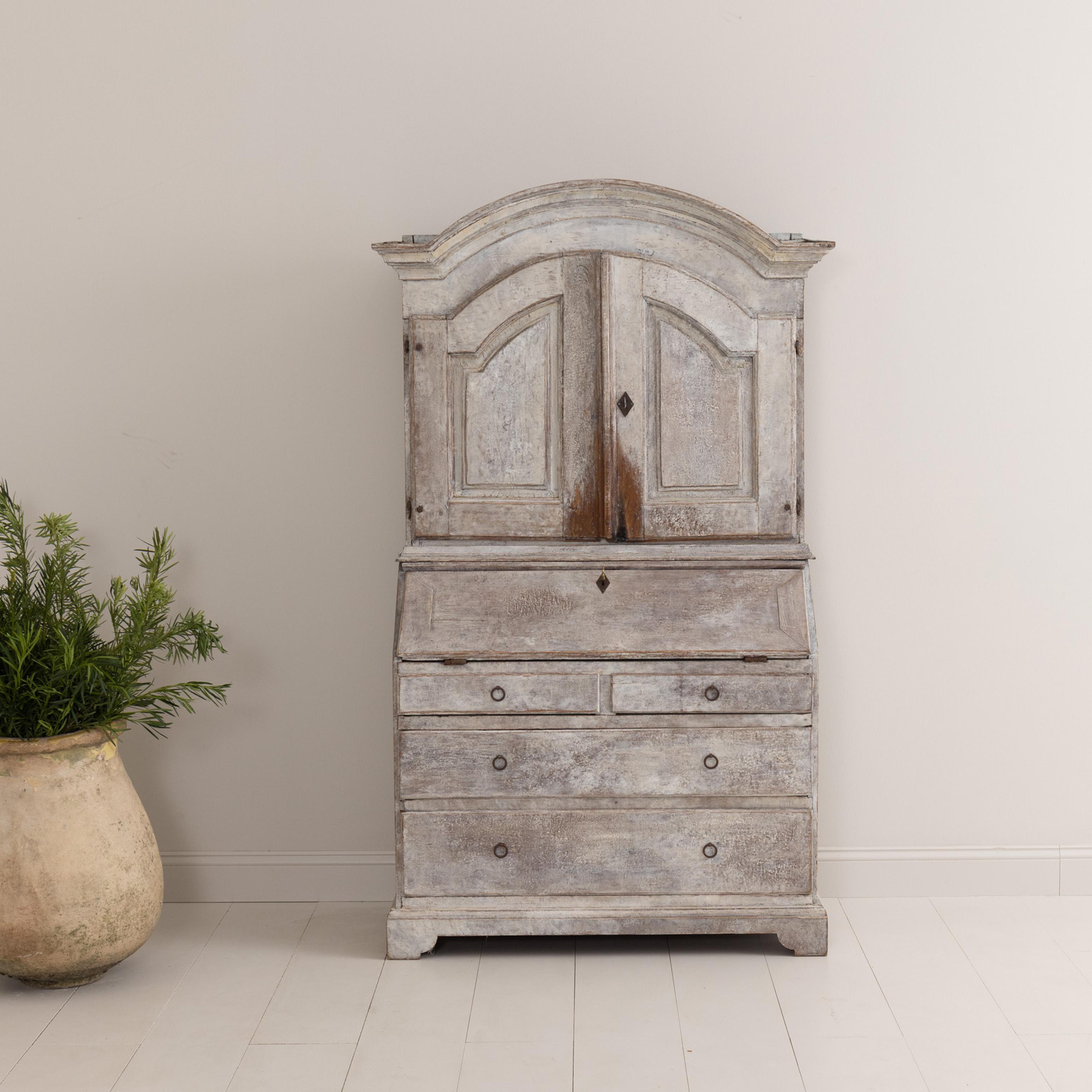 A Swedish slant-front secretary from the 18th century in two parts with arched cornice and bracket base. Found in Kronoberg in southern Sweden, an area known for crystal and furniture. Baroque period, circa 1750. The paint has been hand-scraped down