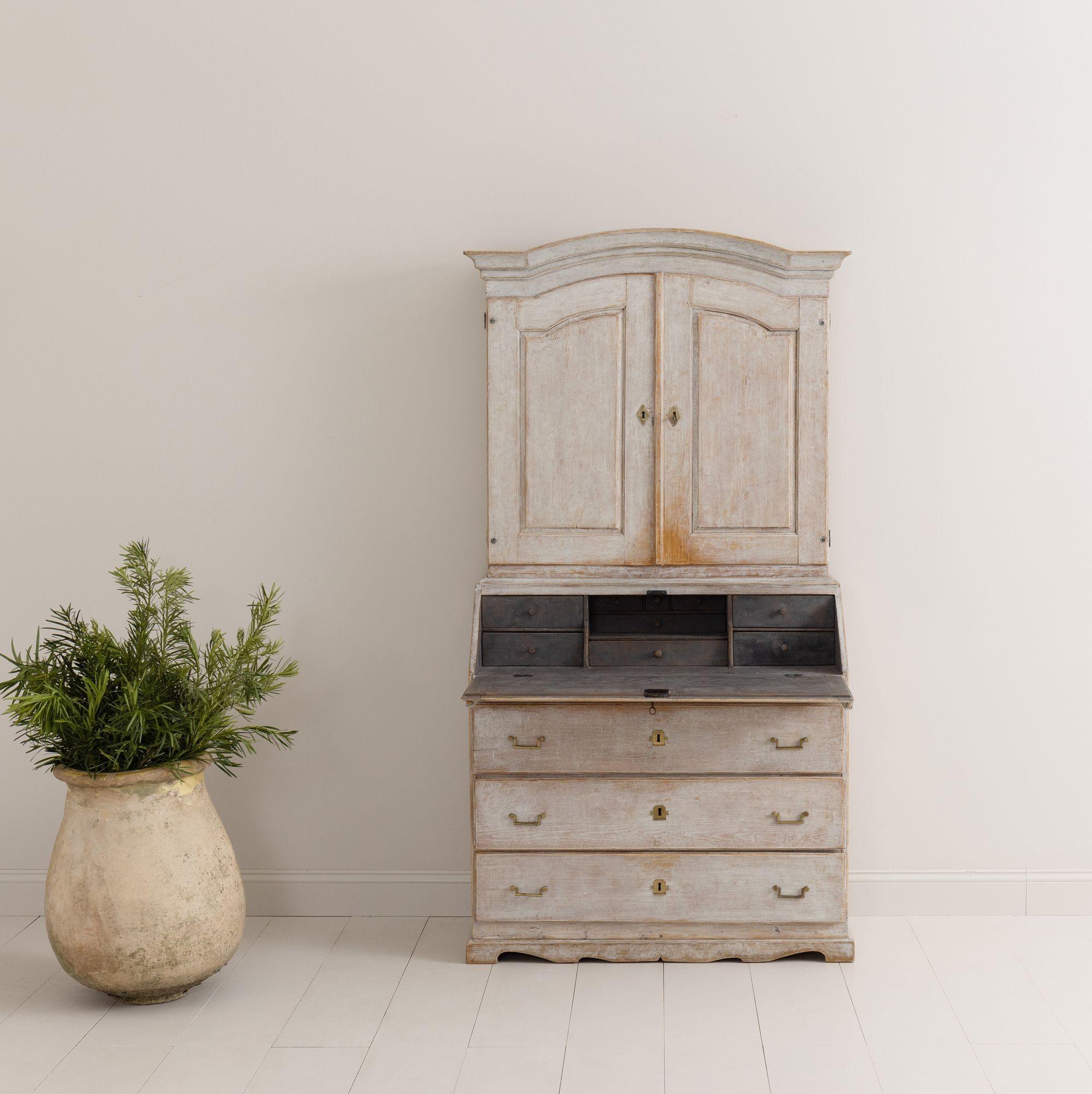 A Swedish early Gustavian period secretary with library from the 18th century with shaped cornice, scalped apron, and original bronze hardware. The upper section has four fixed shelves, the top slotted for utensils. The slant front opens to reveal