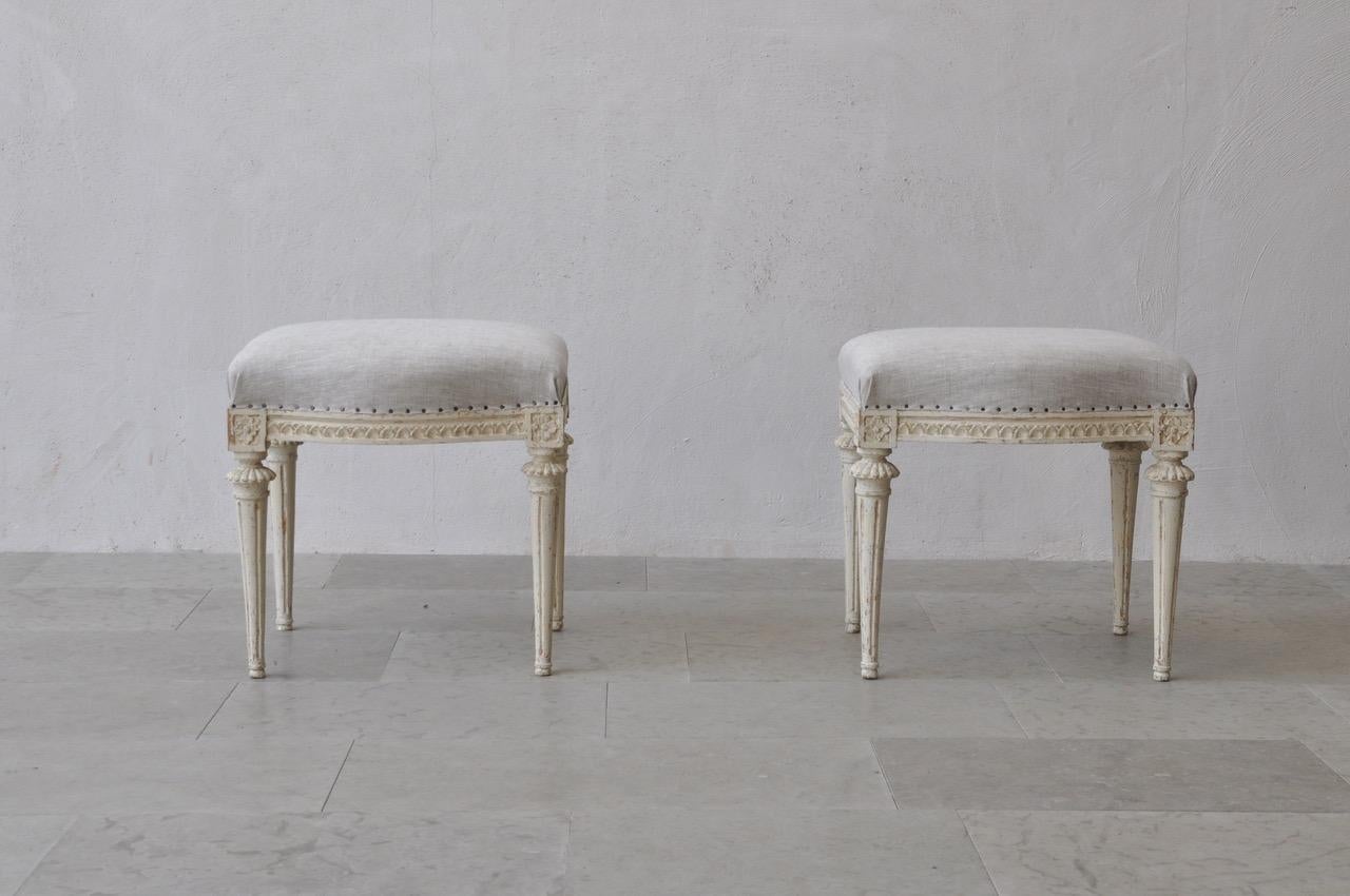 A beautiful pair of Swedish footstools from the Gustavian period signed by Melchior Lundberg (MLB), 1775-1812. These stools are wearing their original paint. There is carved egg and dart detail on the seat frame with rosettes on the corner posts.