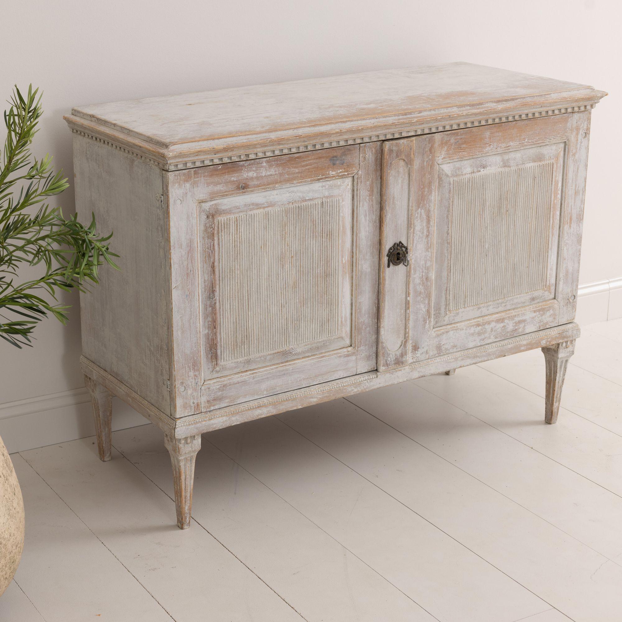A rare 18th century Swedish buffet from the Gustavian period, dry scraped back to reveal the original white paint and natural wood surface. This beautiful buffet has dentil molding around the top, two large reeded doors, and is raised upon elongated