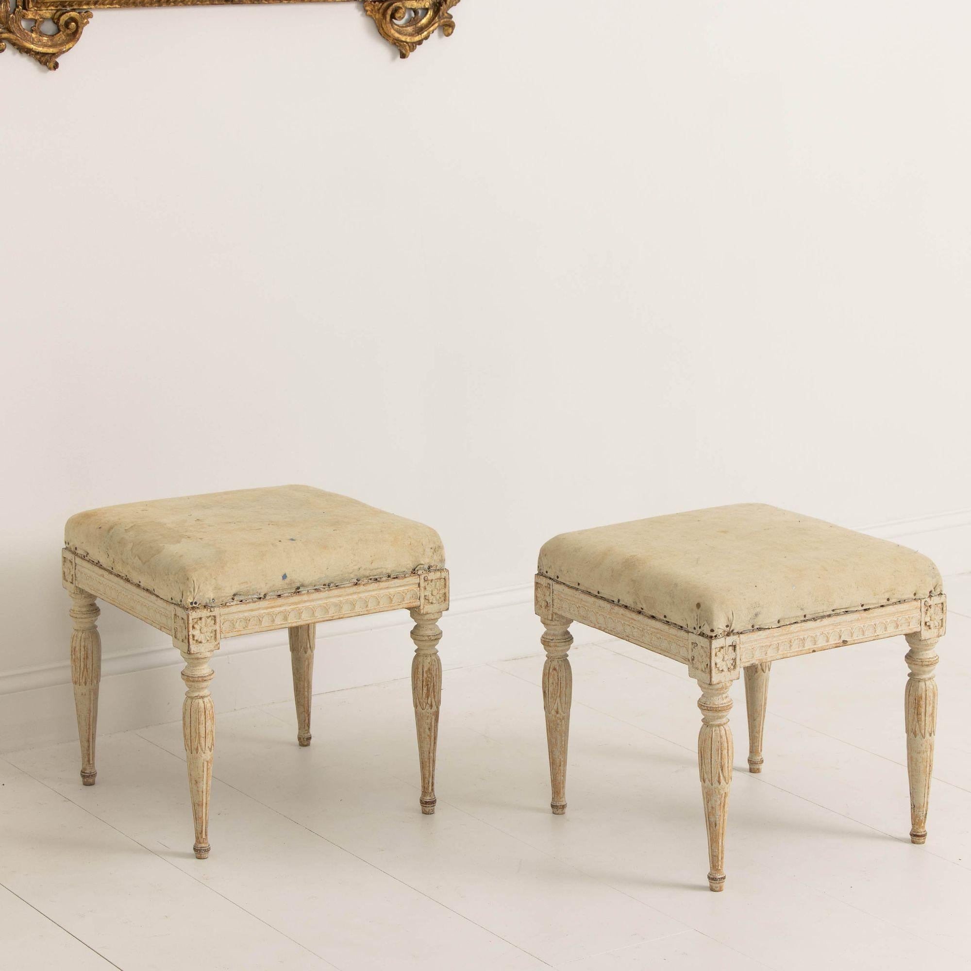A charming pair of Swedish benches from the early Gustavian period in original paint, circa 1780. These stools display beautiful carved egg and dart detail on the seat frame, rosettes on the corner posts, and acanthus leaves on round, tapered legs.