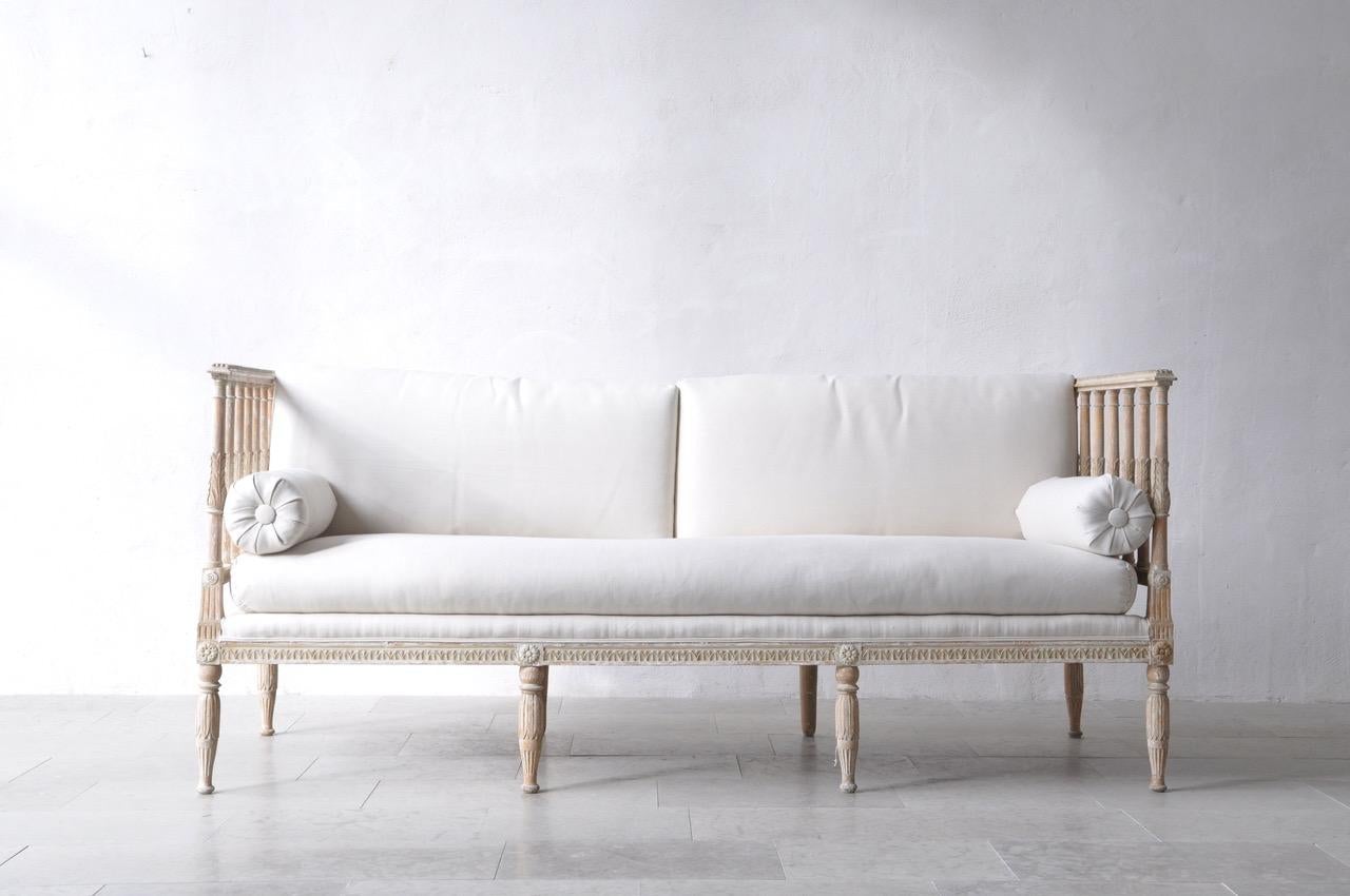 An 18th century Swedish Gustavian period daybed made in Stockholm. This beautiful, circa 1790 daybed has been hand-scraped to reveal the original paint surface and newly upholstered in linen with side bolster pillows. Baluster sides with carved