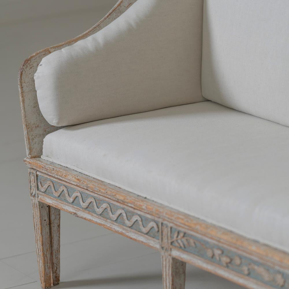 A stunning period Swedish tragsoffa wearing blue - gray paint, newly upholstered in linen. The seat extends out converting the sofa to a bed. This piece has the most beautiful and unusual wood carvings around the seat frame and is raised up tapered