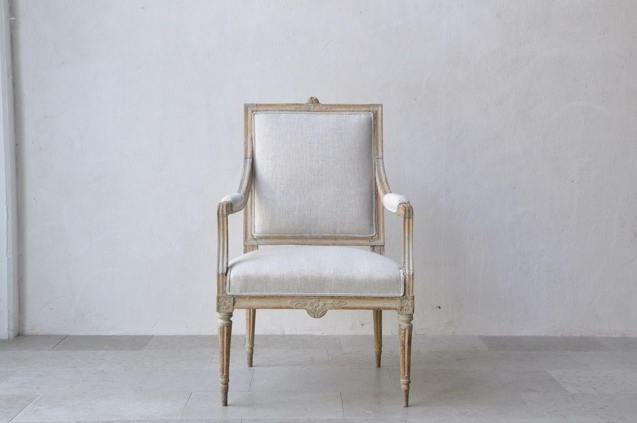 A Swedish armchair from the Gustavian period in Stockholm quality, hand-scraped to the original paint and newly upholstered in linen. Exquisitely carved floral and leaf motif on the back and seat frame. Beautifully tapered and fluted legs with