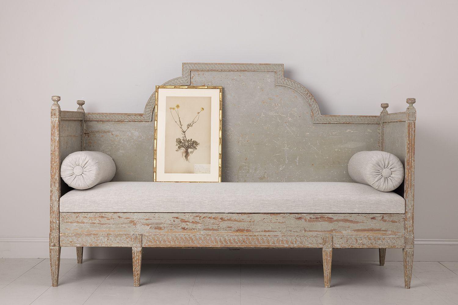 A Swedish daybed sofa from the Gustavian period dry-scraped to reveal the original paint and newly upholstered in linen with side bolster pillows. This sofa or banquette is beautifully hand carved with a guilloché detail around the back and seat