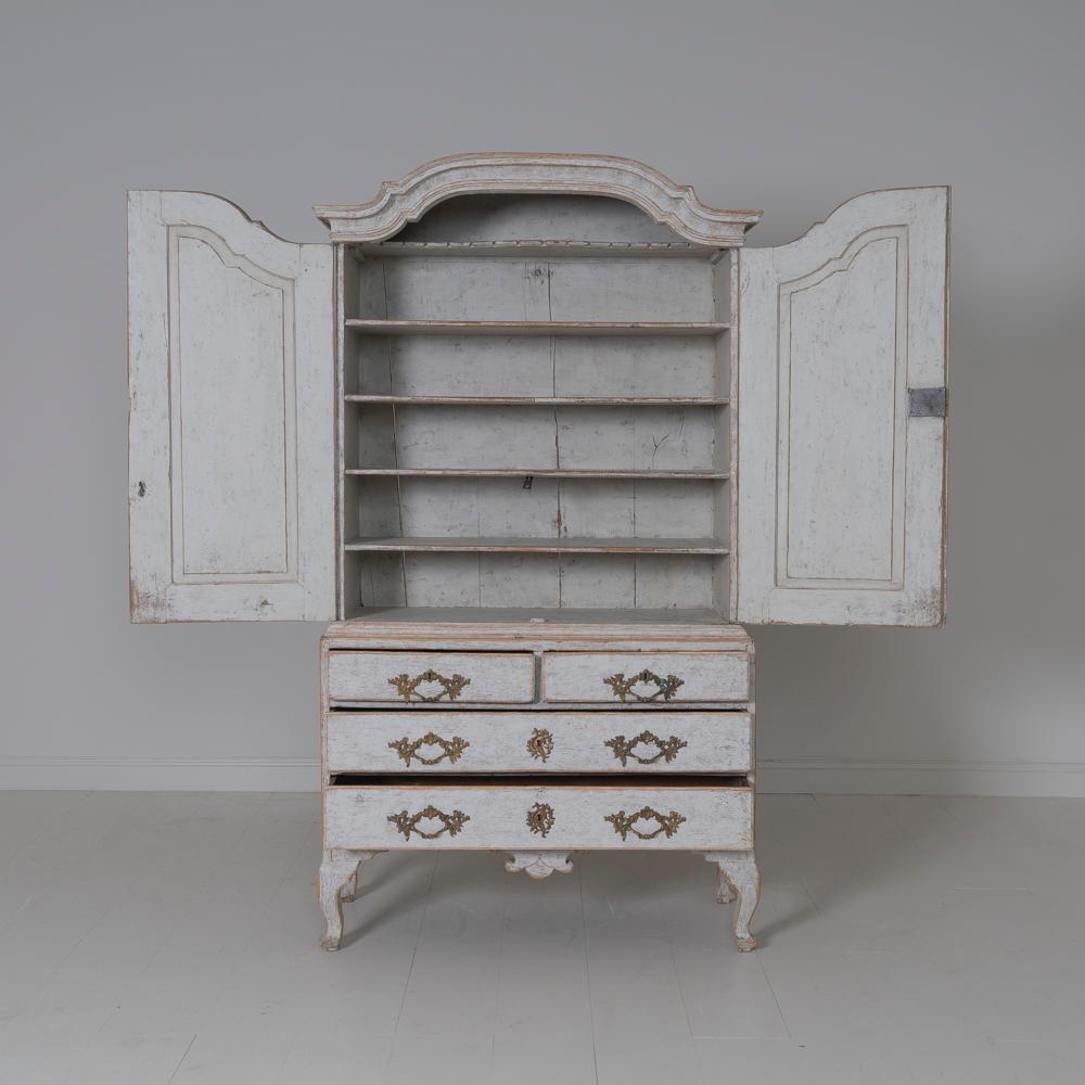 An 18th century two-part Swedish linen press or armoire from the Rococo period with original bronze hardware, locks, and keys. This cabinet is beautifully proportioned with a gracefully arched pediment cornice and curvaceous cabriole legs. The
