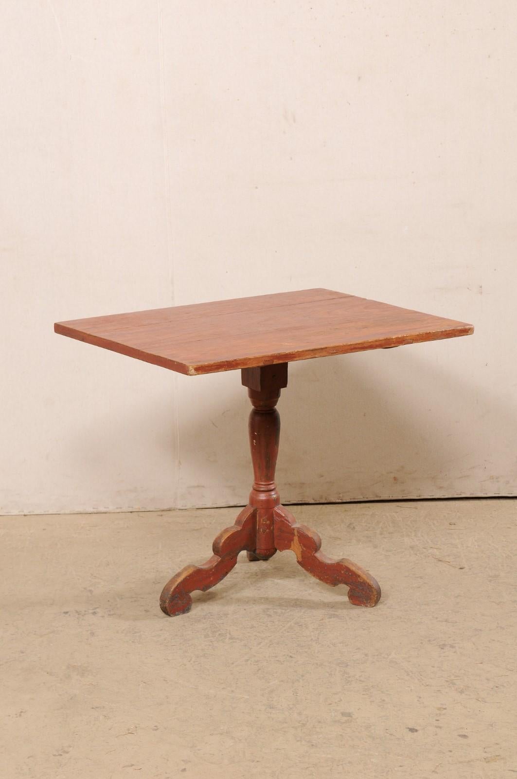 A Swedish tilt-top table with its original paint from the 18th century. This antique table from Sweden features a rectangular-shaped tilt top which rests upon a delicately turned central pedestal column that terminates into a raised tripod base