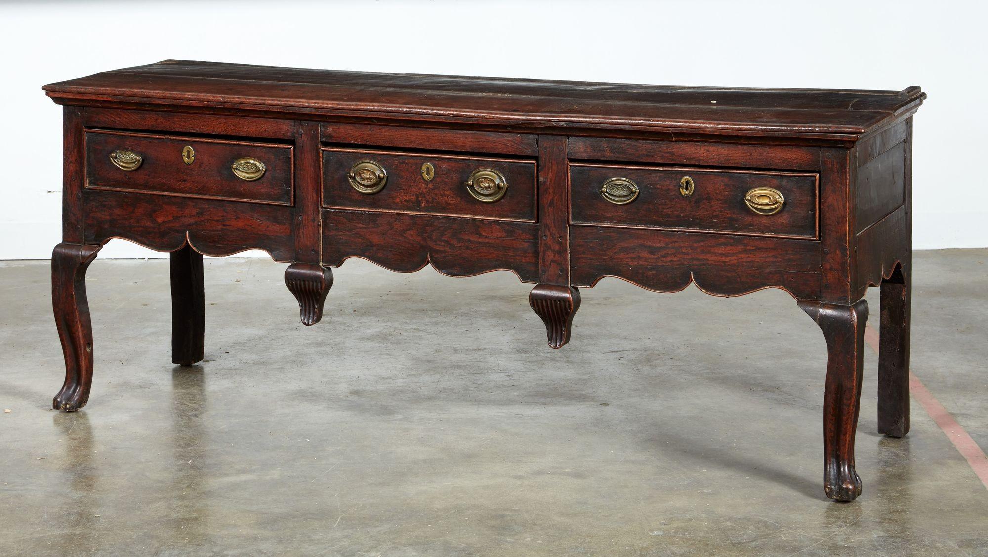 A vernacular three drawer low dresser or sideboard with a great presence. Made of richly colored oak by a regional country craftsman basing styling on London furniture designs then in vogue, including ogee molded edged top over shaped apron with