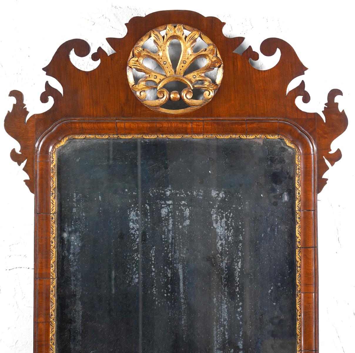 This fine English George II fret carved mirror dates to circa 1750 and features the original plate in a carved giltwood filet and a fret carved mahogany frame carved with ears and scrolls centering a circular pierced giltwood leaf in the crest and