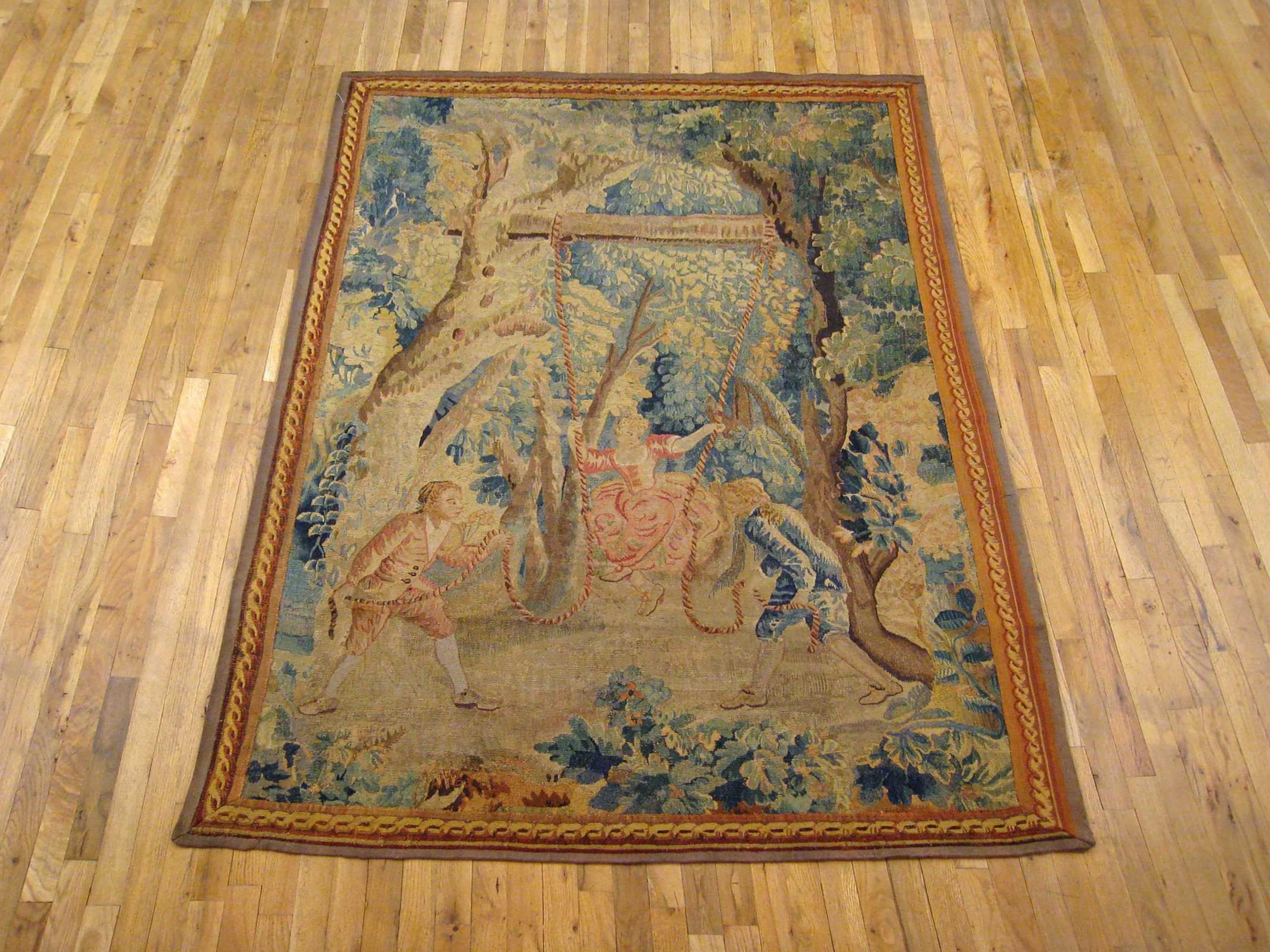 A Flemish rustic tapestry from the 18th century, depicting a charming scene with two young noblemen pulling a young damsel on a swing within a verdant courtyard setting. Enclosed by an elegant ribbon-twist border. Wool with silk inlay. Measures: