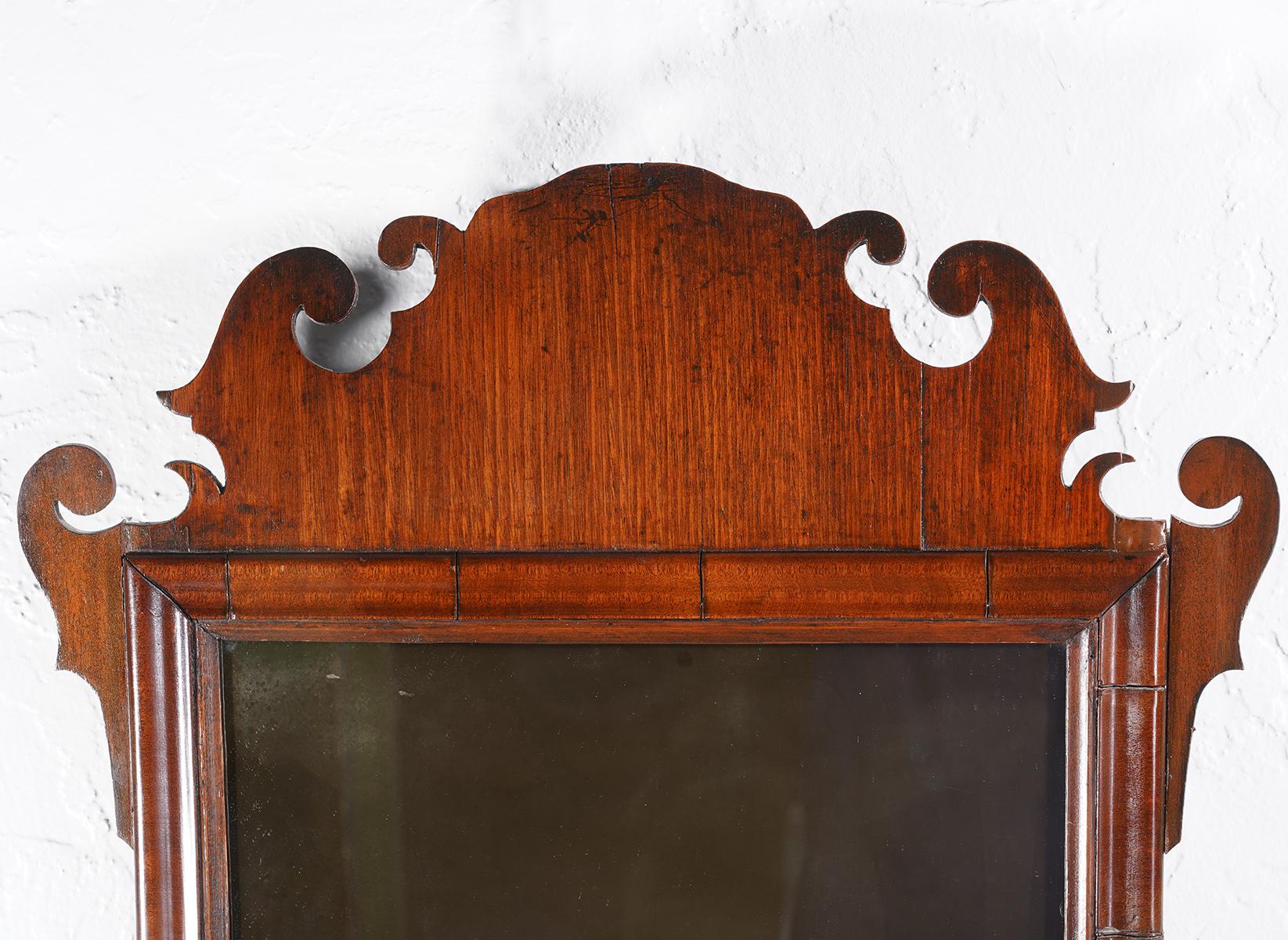 This English Georgian smaller size wall mirror dating to circa 1780 features the plate set in a fret carved mahogany frame with ears and scrolls on the crest as well as the apron.