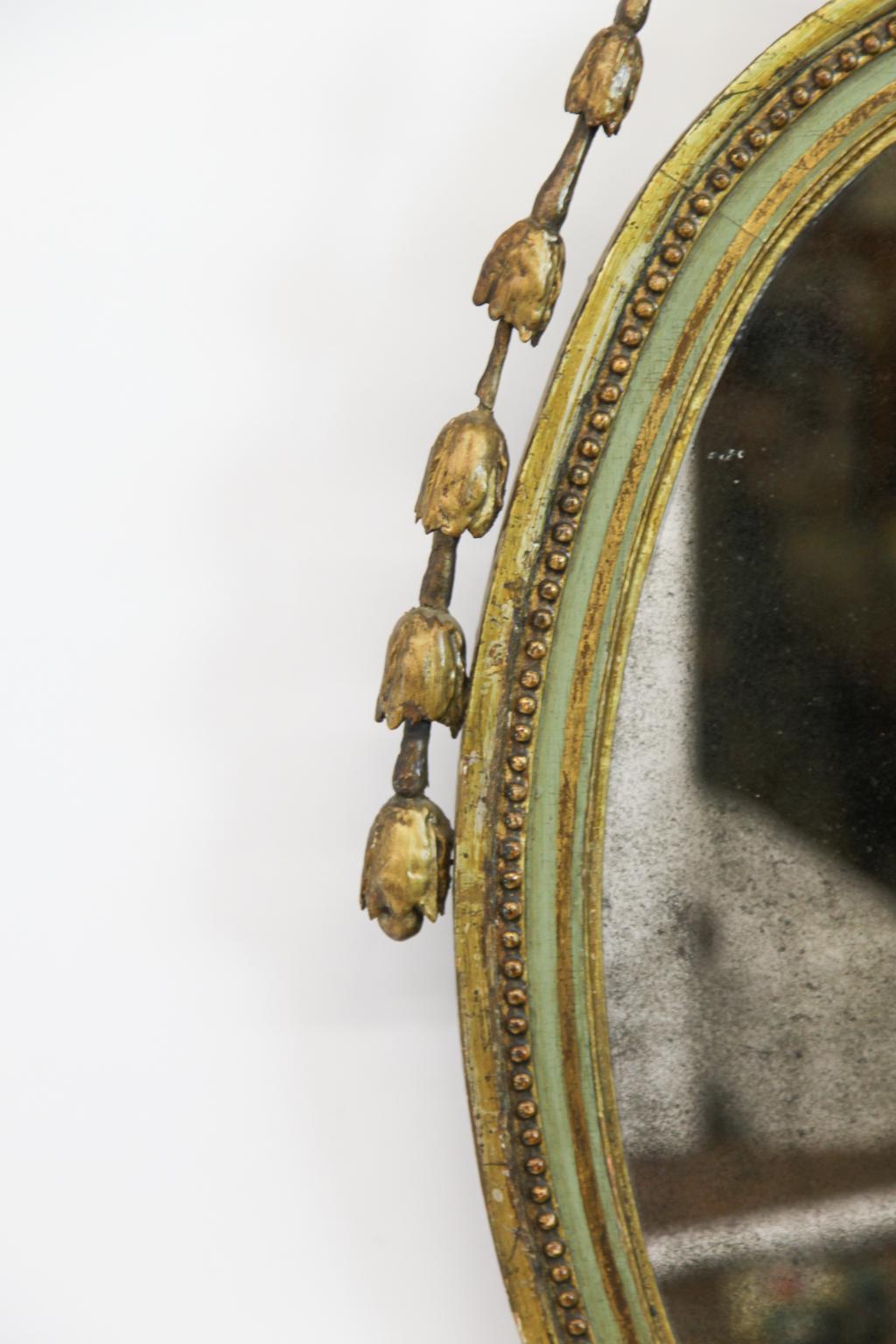 18th century Adam mirror, crowned with gilded urn with arabesque vine scrolls adorned with bellflower and foliate, the oval painted and gilded wood frame with foliated arabesques and bellflower motif below.