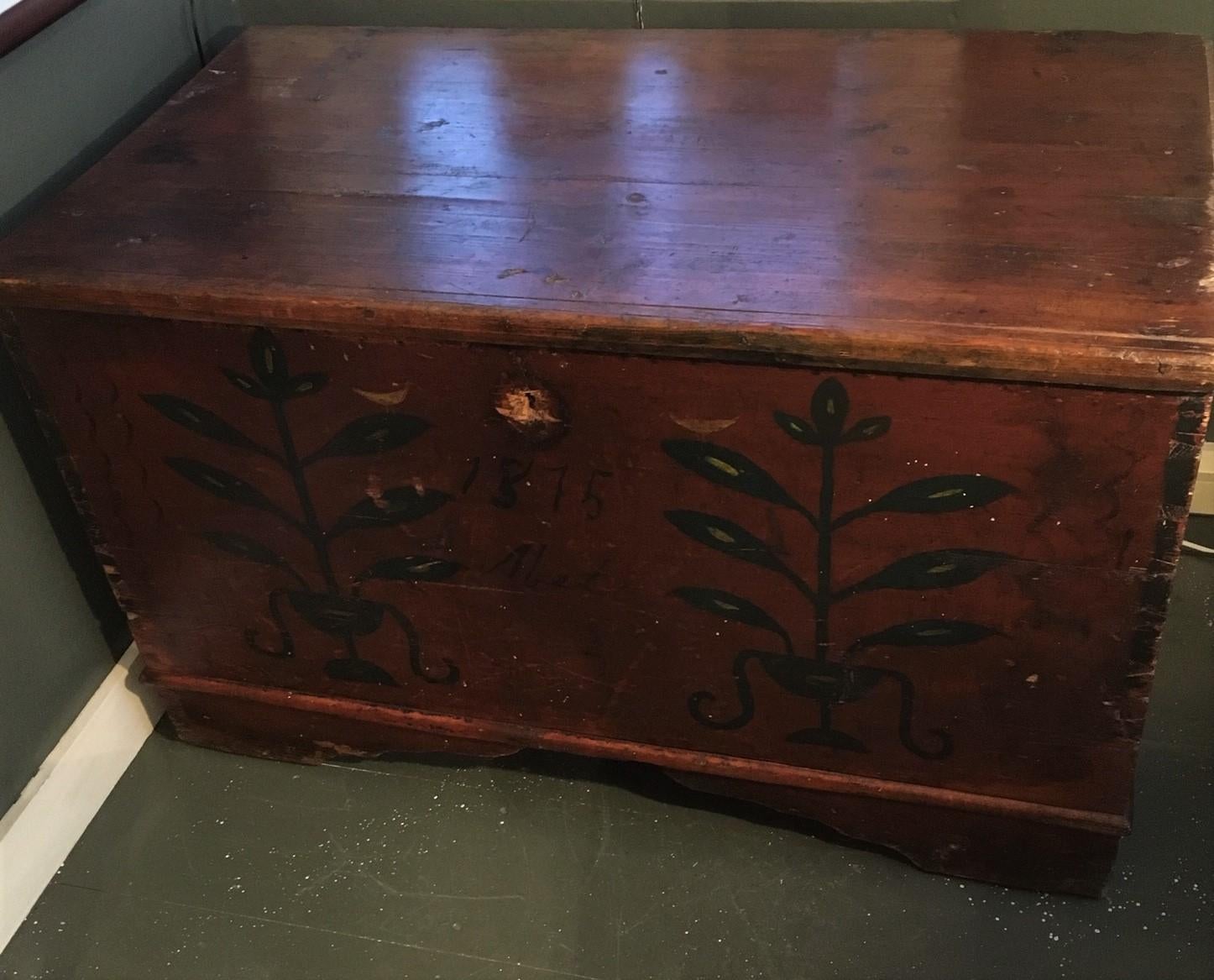 18th century American pine decorated blanket chest, probably from New England, circa 1770 having a dovetailed case on wide bracket feet, the lid held by long strap hinges; in original red paint with later green painted foliage decorations with