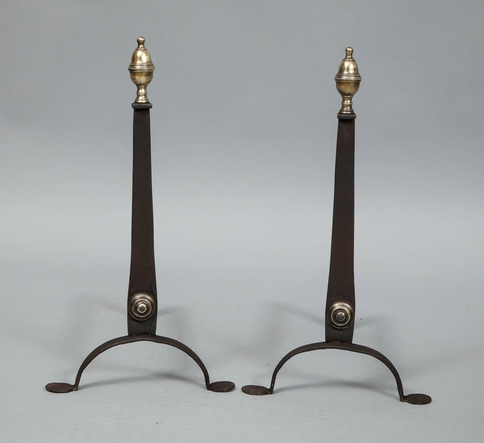 A pair of 18th century andirons with knife blade shafts having brass urn finials and shaft buttons standing on arched legs with penny feet, American, circa 1770.
 
