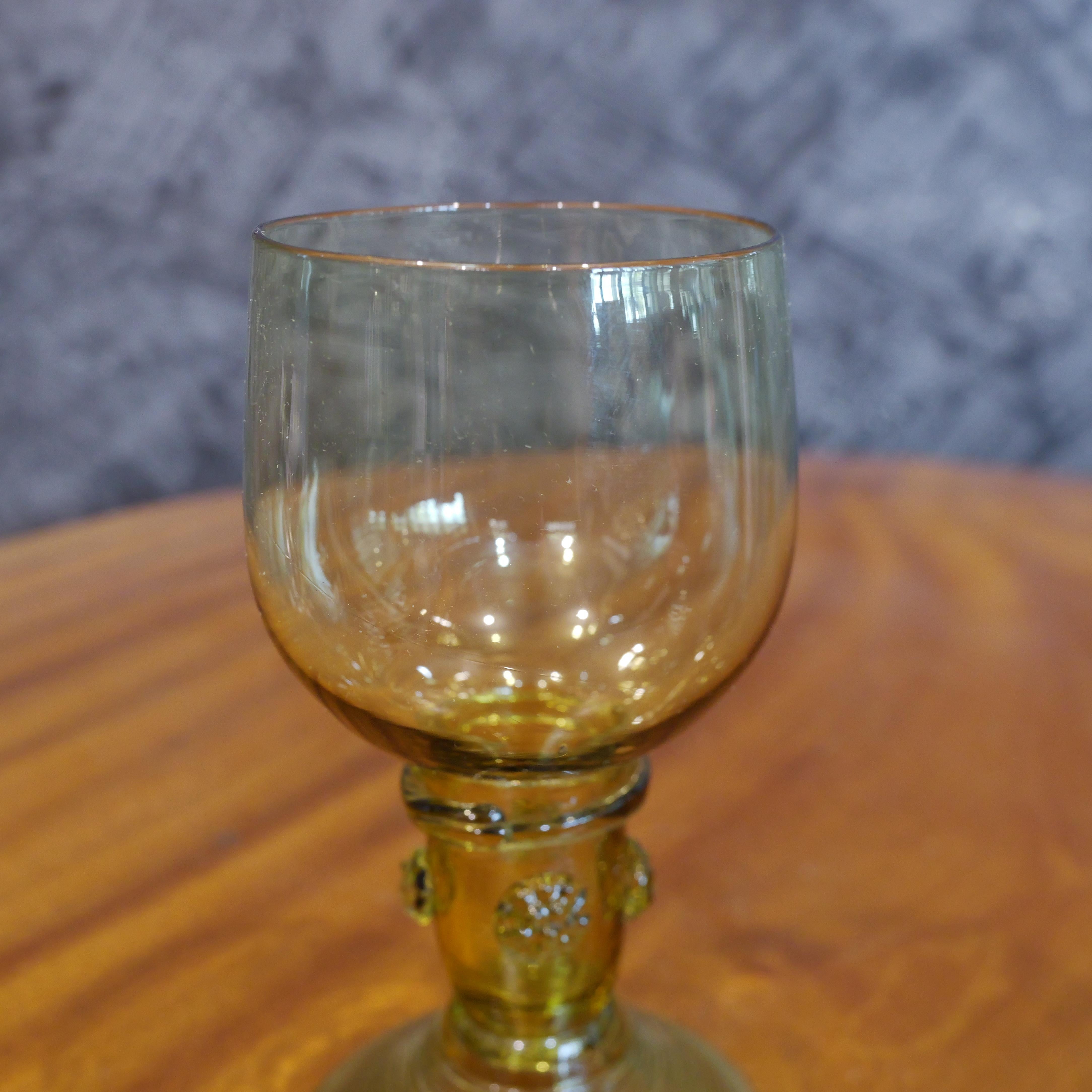This 18th-century amber wine glass embodies the elegance and craftsmanship of the era. Its exquisite design features an ovoid bowl, delicately balanced atop an open, hollow stem. This unique stem design served a practical purpose, allowing sediment