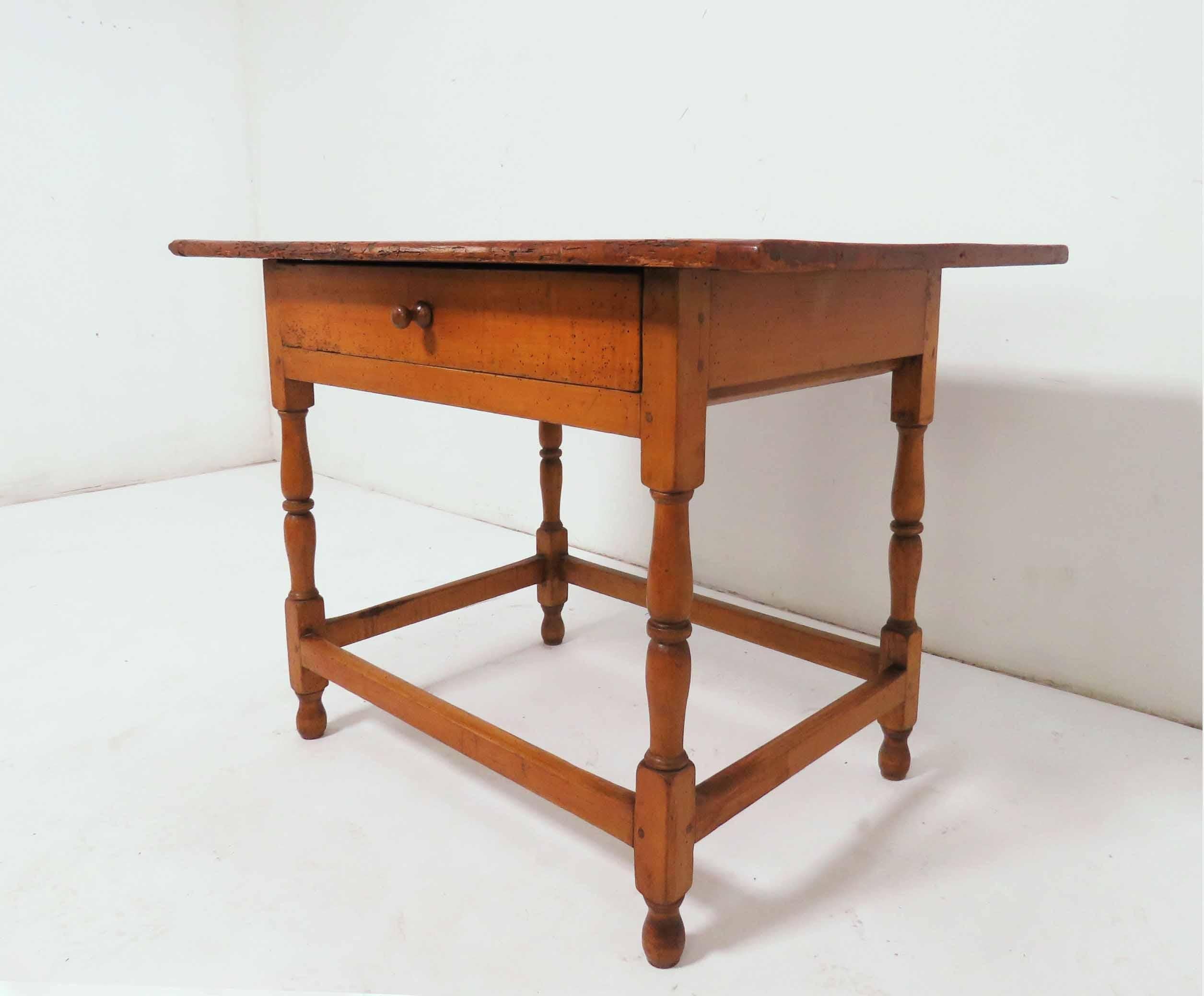 An 18th century American tavern table in pine with a single drawer and a breadboard top.