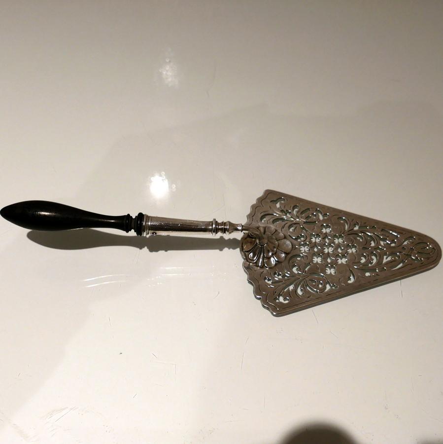 A delightful Georgian silver cake slice decorated with beautiful intricate hand piercing to the blade/scoop. The slice is designed with a stylish contrasting mix of ornate (lower section) plain formed tubing (middle section) and shaped fruitwood