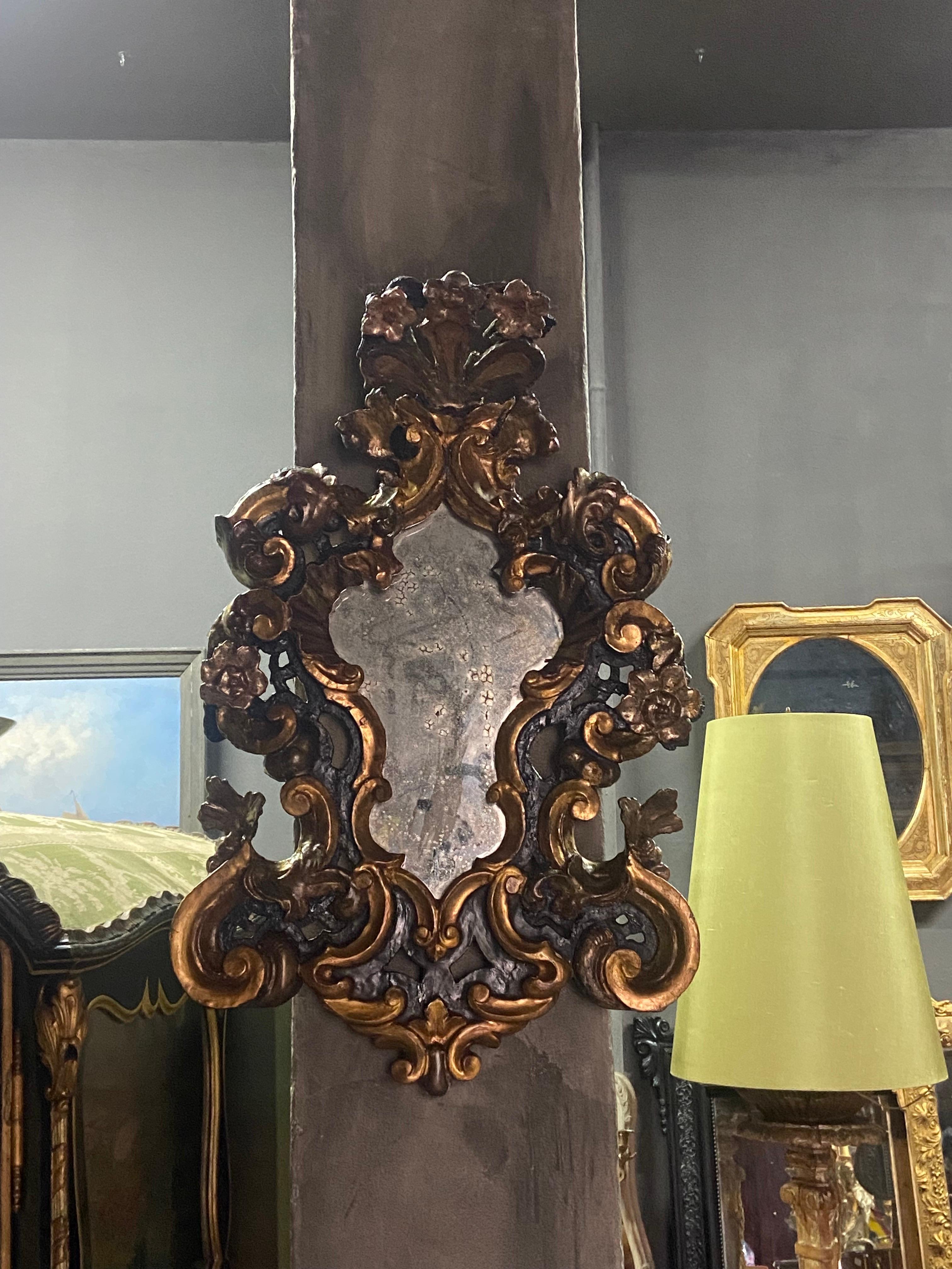 Exquisite Italian wall mirror made in hand carved wood with gilded parts and floral motifs still wearing the original glass. There was some restorations in order all parts to be well fixed but it still wears the original painting. Extremely