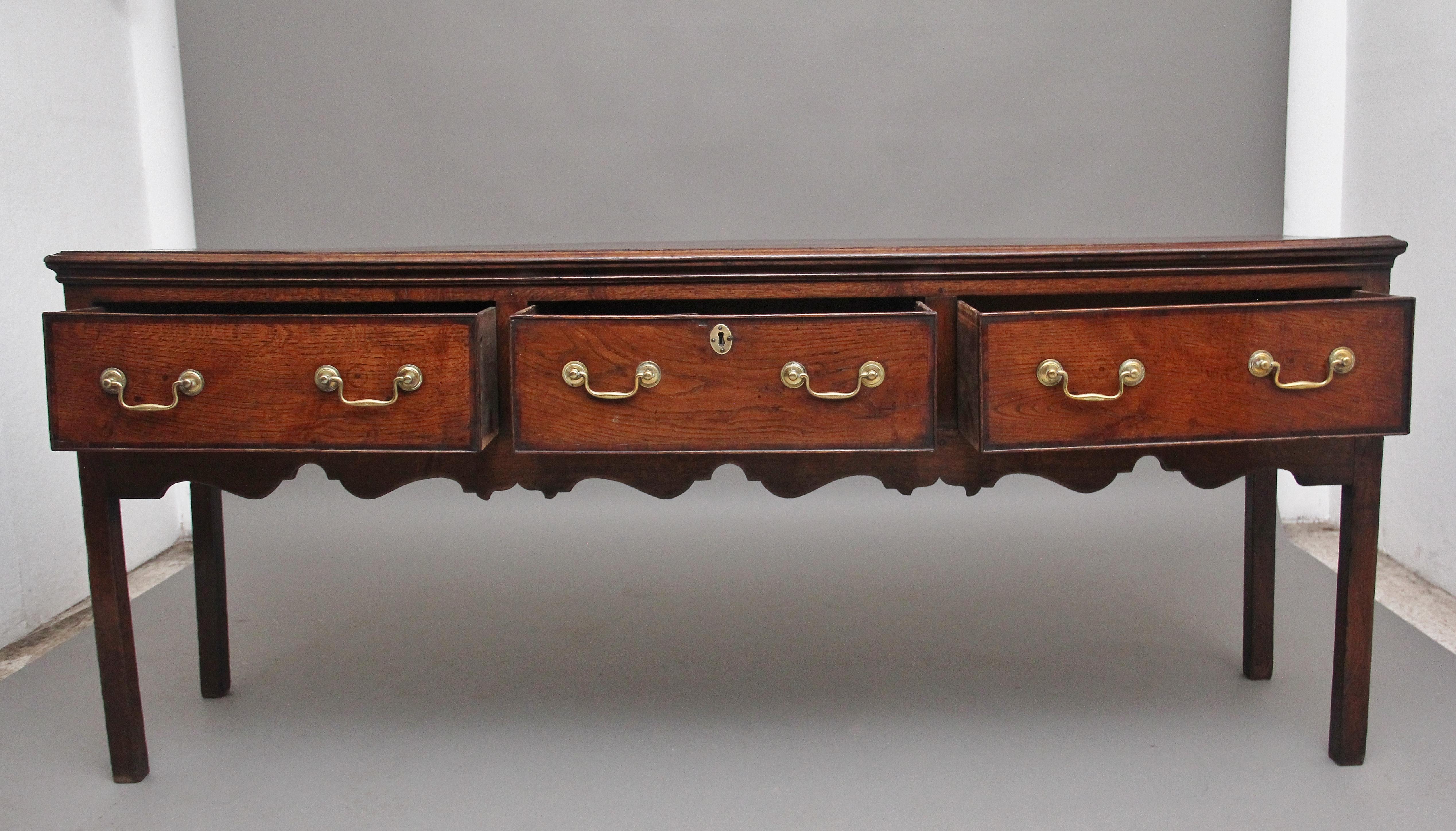 A superb quality 18th century oak dresser base, having a lovely figured top with a thumb moulded edge above three deep oak lined drawers with the original brass swan neck handles, crossbanded on the drawer fronts, with a decorative shaped frieze