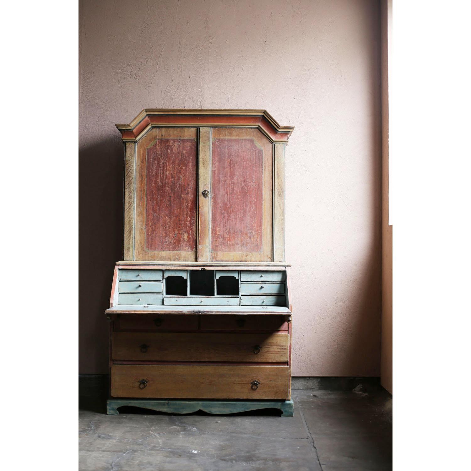 A two-tiered wooden cabinet from the 18th century Swedish Gustavian period. The top door opens to reveal a decorative top shelf and three other shelves. The top of the bottom shelf can be opened forward to use as a small counter. There are also many
