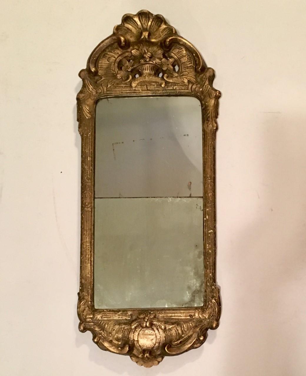 This is an excellent 18th century gilded and ornately carved wooden wall mirror with beautiful Gesso ornaments. It is in the original condition with great patina. The glass plate is in the original two parts. It is very difficult to find this rare