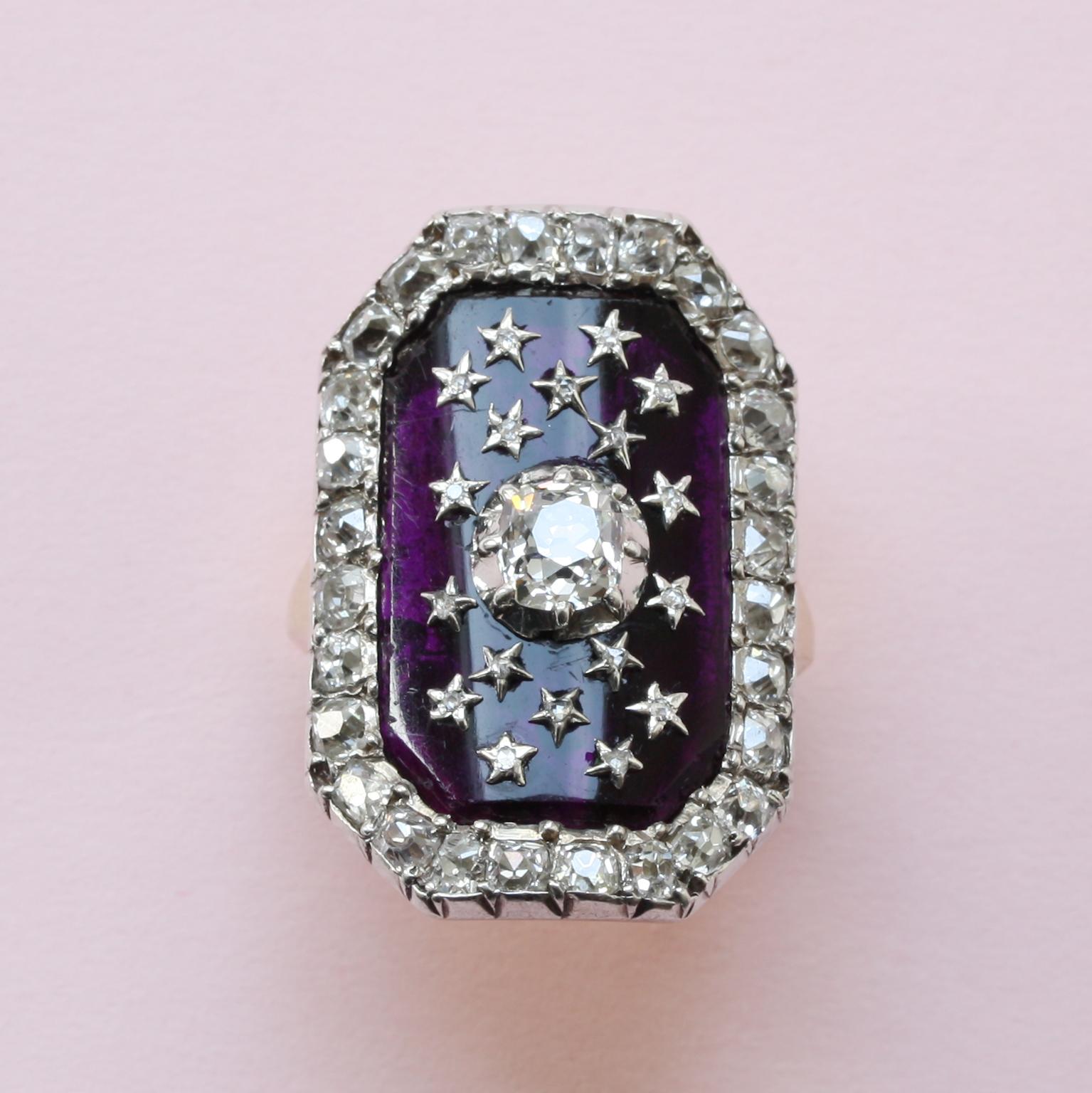 An 18th century gold ring ‘au Firmament’ set with an octagonal purple glass panel and a central cushion cut diamond. The panel is decorated by 18 small silver stars each set with a small rose cut diamond with a border of 28 cushion cut diamonds,