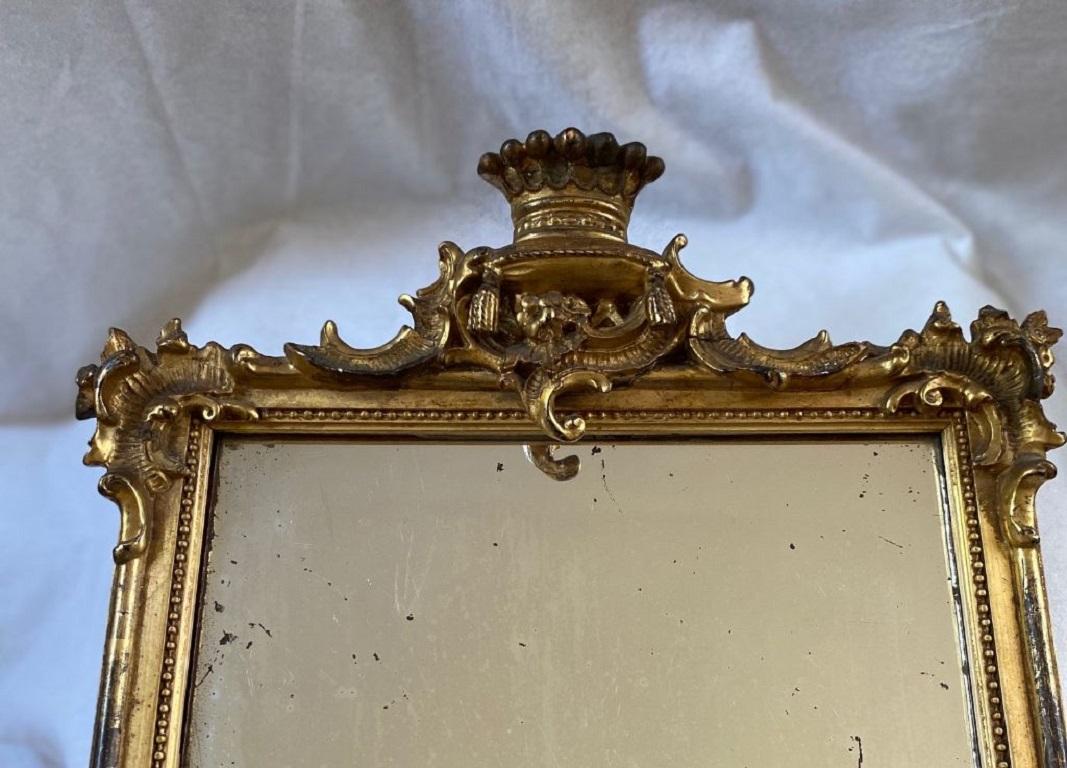 18th century Baroque carved and gilded looking glass, almost certainly English, circa 1740, having a carved crown resting atop a Tassled cushion, with Tudor rose, above a rectangular frame with applied scrolls, acanthus leaves and cockbeading around